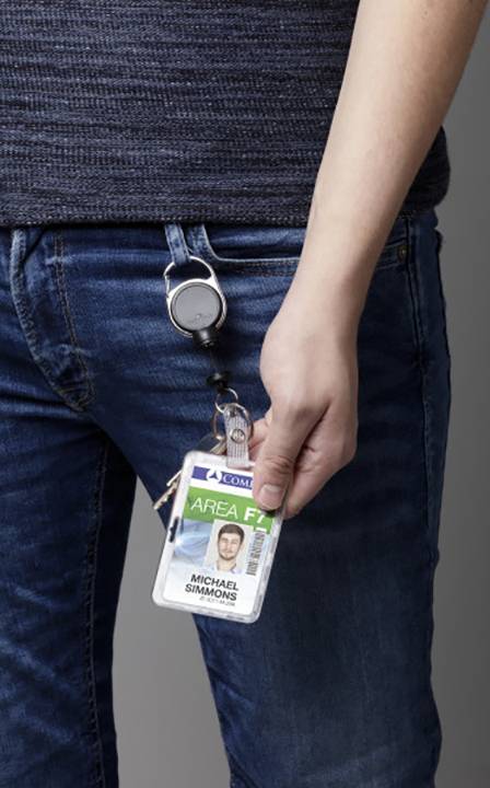 Une personne tient une carte d'identité attachée à son jean avec un clip. La carte montre une photo et le nom 