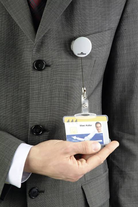 Une personne en costume tient une carte d'identité à la main. La carte est fixée avec un clip sur le revers de la veste.