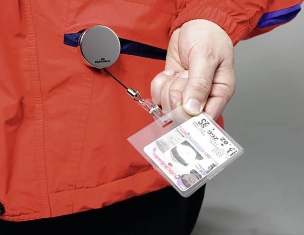 Une main tient un badge nominatif attaché à un cordon rétractable accroché à une veste rouge.