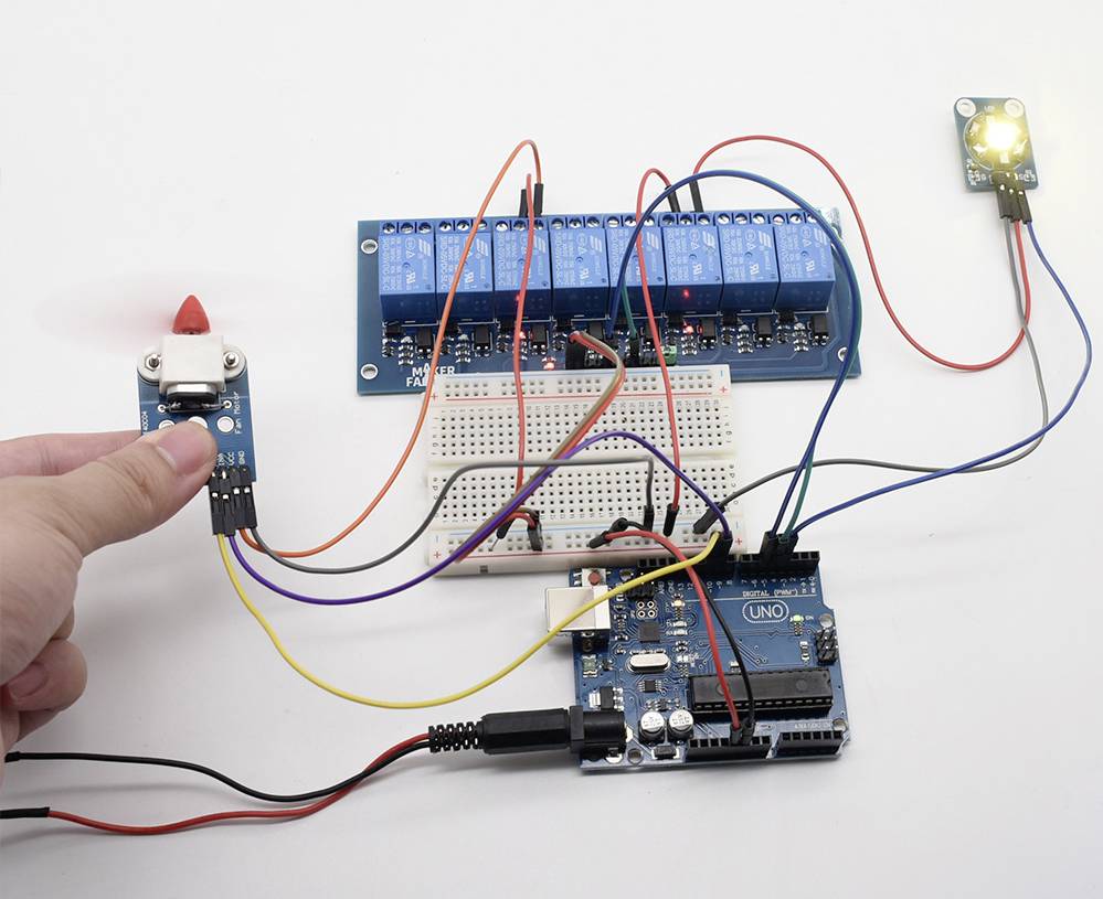 Une main tient un capteur, connecté à un circuit électronique. Différents fils mènent à une carte de contrôle ; un voyant LED est allumé à droite.