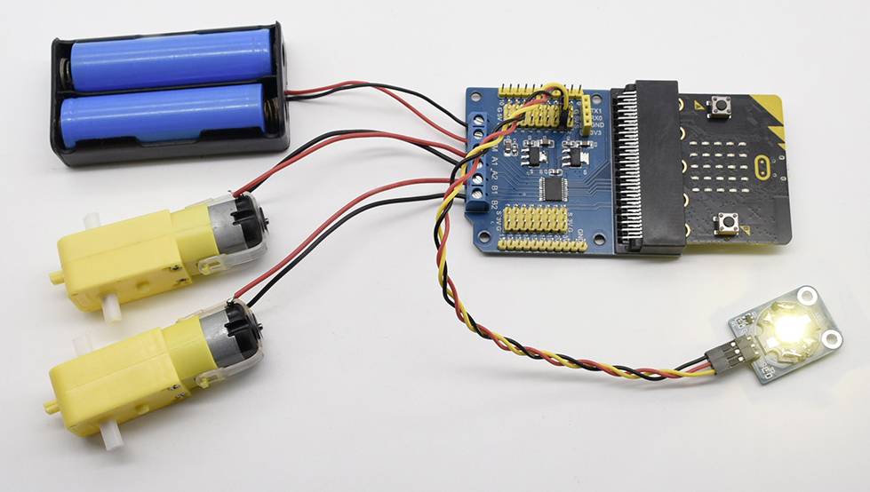 Un circuit simple avec un microcontrôleur, deux moteurs jaunes, un support de batterie avec deux piles et une LED lumineuse.