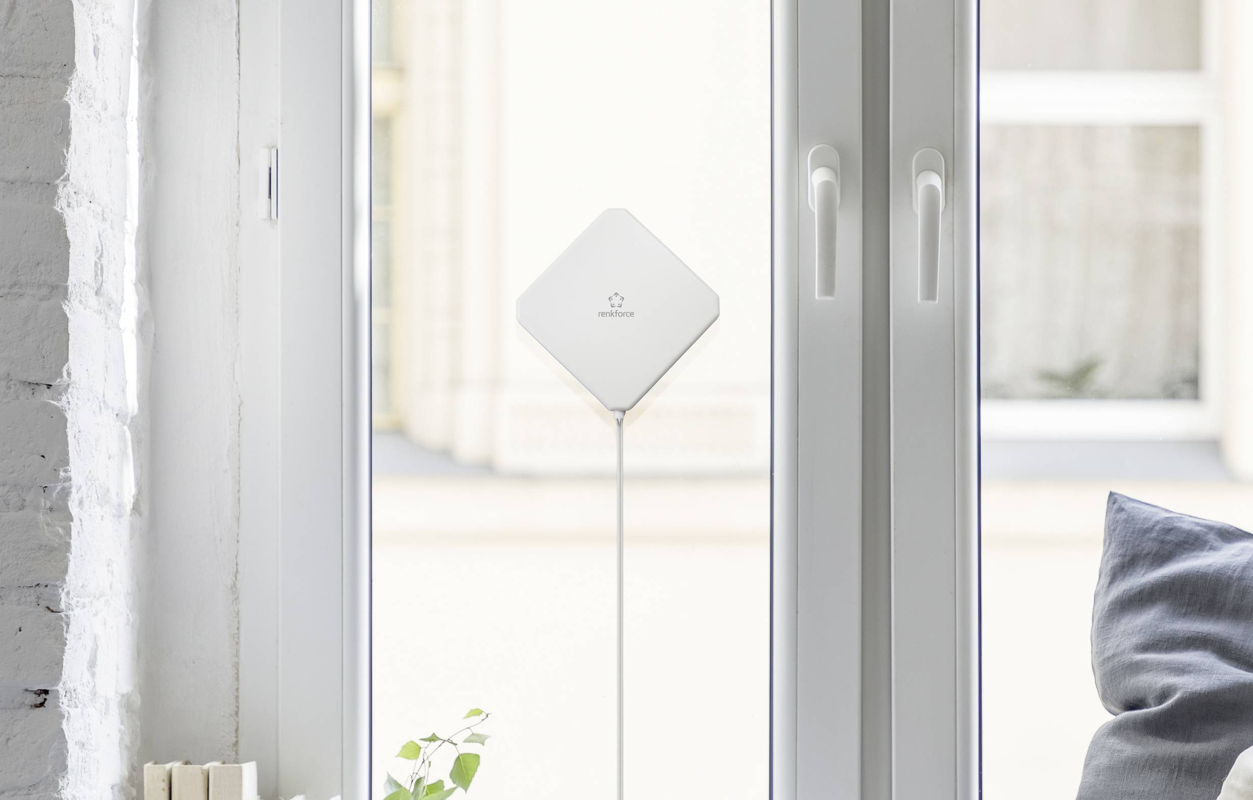 Un appareil technique blanc est placé devant une grande fenêtre. Il est rectangulaire et fixé à une tige fine. Des volets sont visibles en arrière-plan.