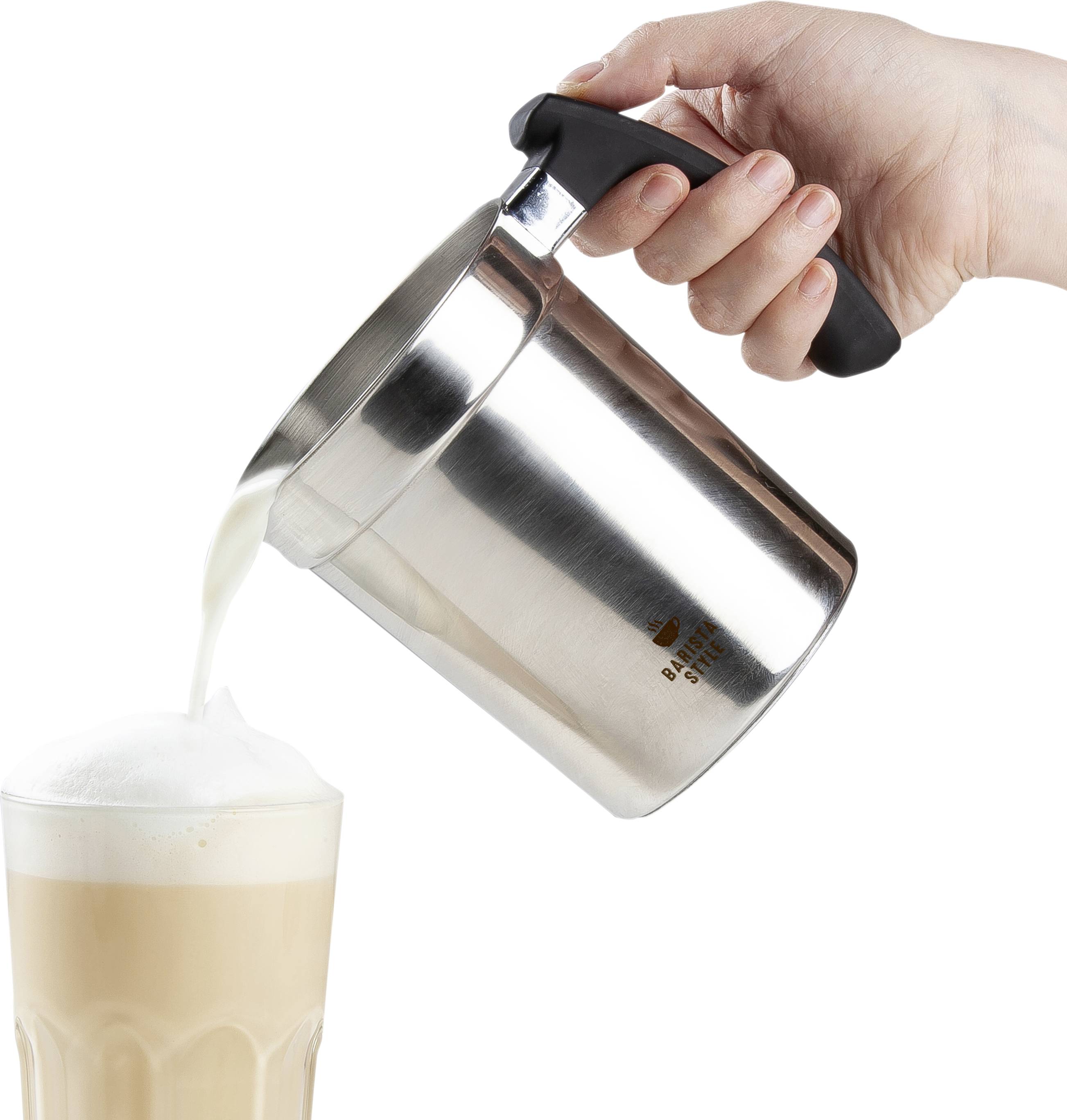 Une main verse de la mousse d'un petit pot à lait en acier inoxydable dans un verre à latte, posé sur une table.