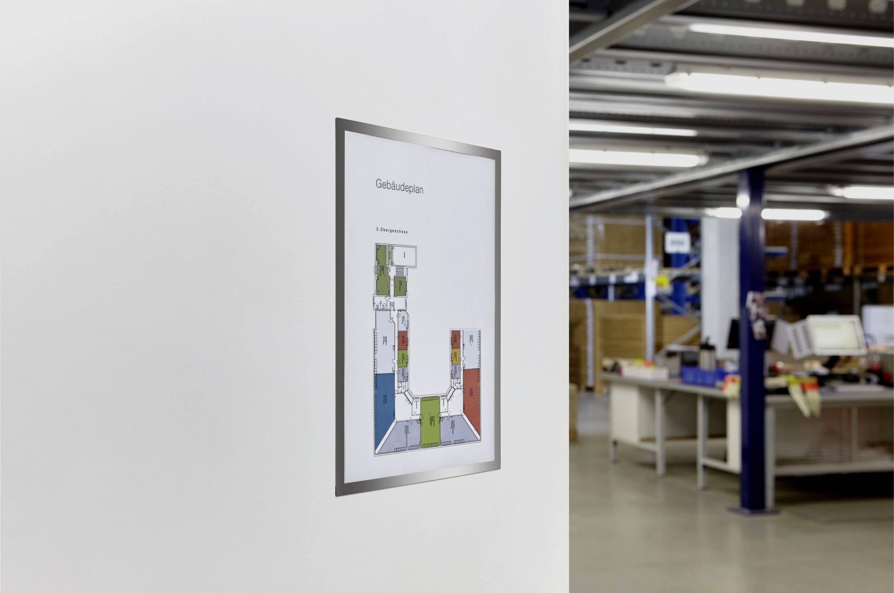 Un plan d'évacuation est accroché à un mur blanc dans un bureau avec des étagères et des postes de travail en arrière-plan.