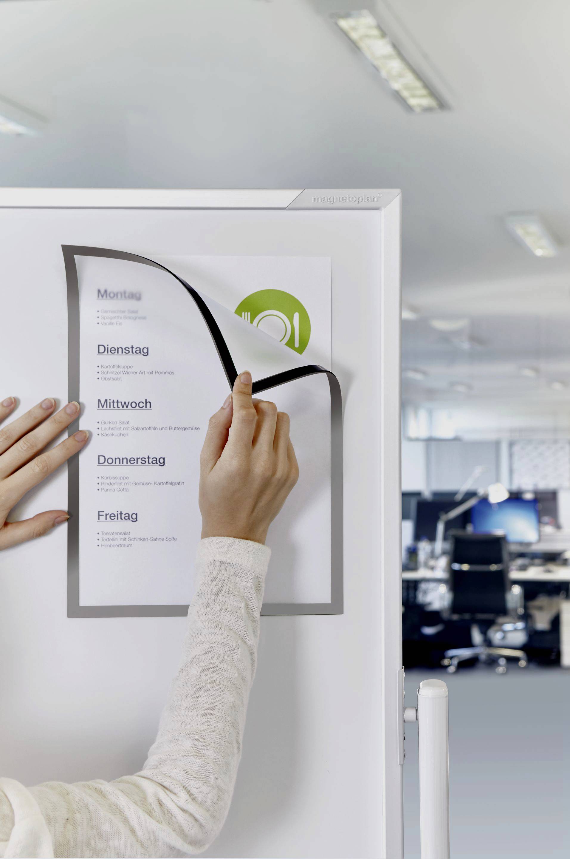 Une personne change une feuille sur un calendrier blanc dans un bureau moderne. Les jours de la semaine sont indiqués sur le calendrier.