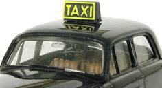 Un taxi miniature noir avec un panneau jaune 'TAXI' sur le toit, vu de l'avant.