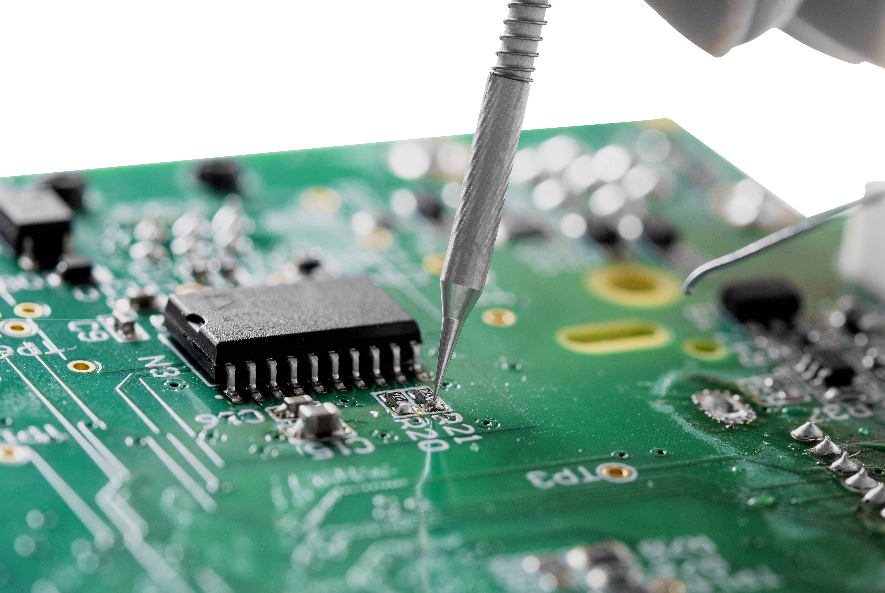 Gros plan d'un circuit imprimé vert sur lequel un fer à souder travaille sur un composant électronique.