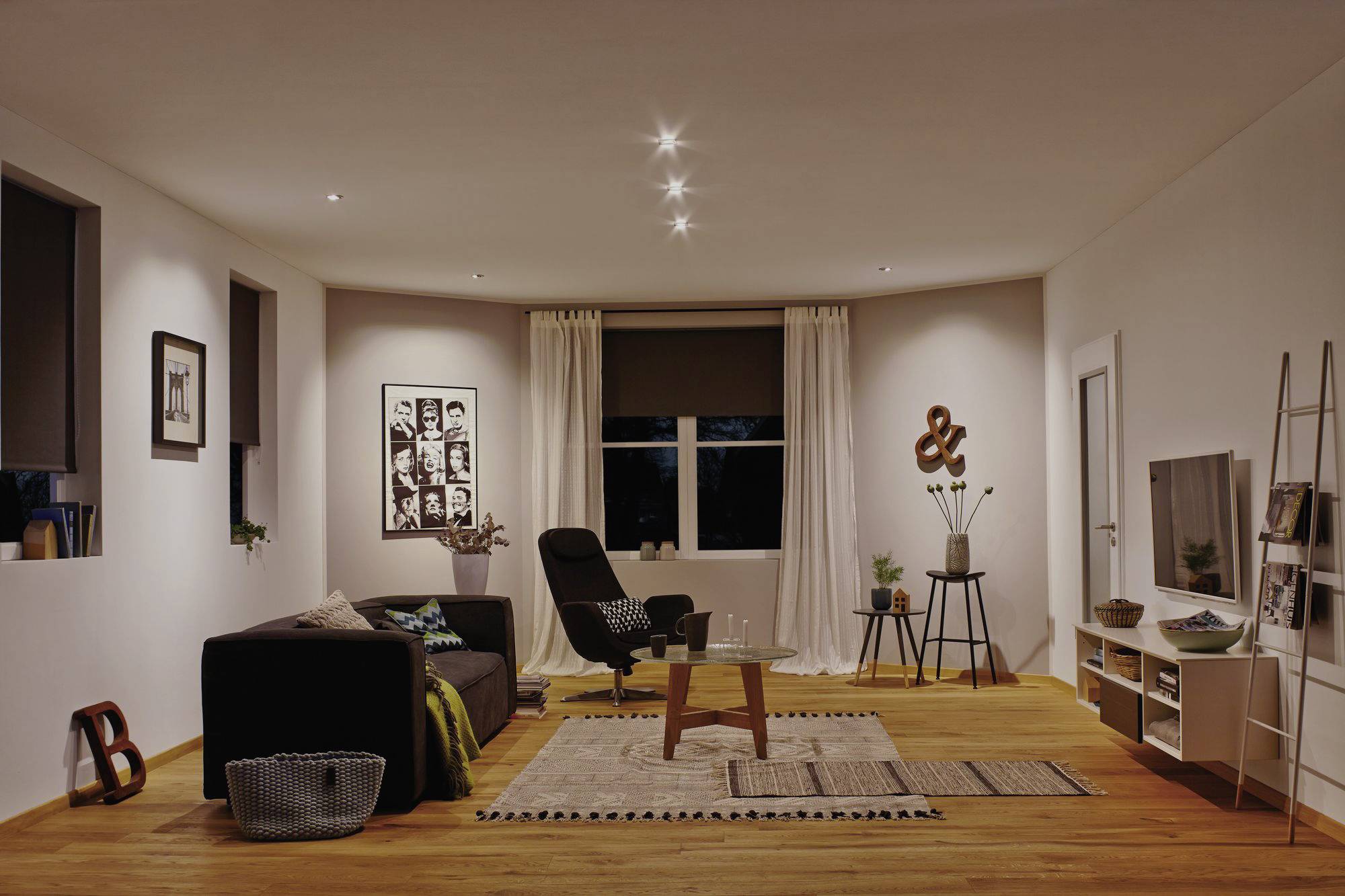 Salon accueillant avec canapé, fauteuil, tapis et décoration. Éclairage tamisé et art moderne aux murs.