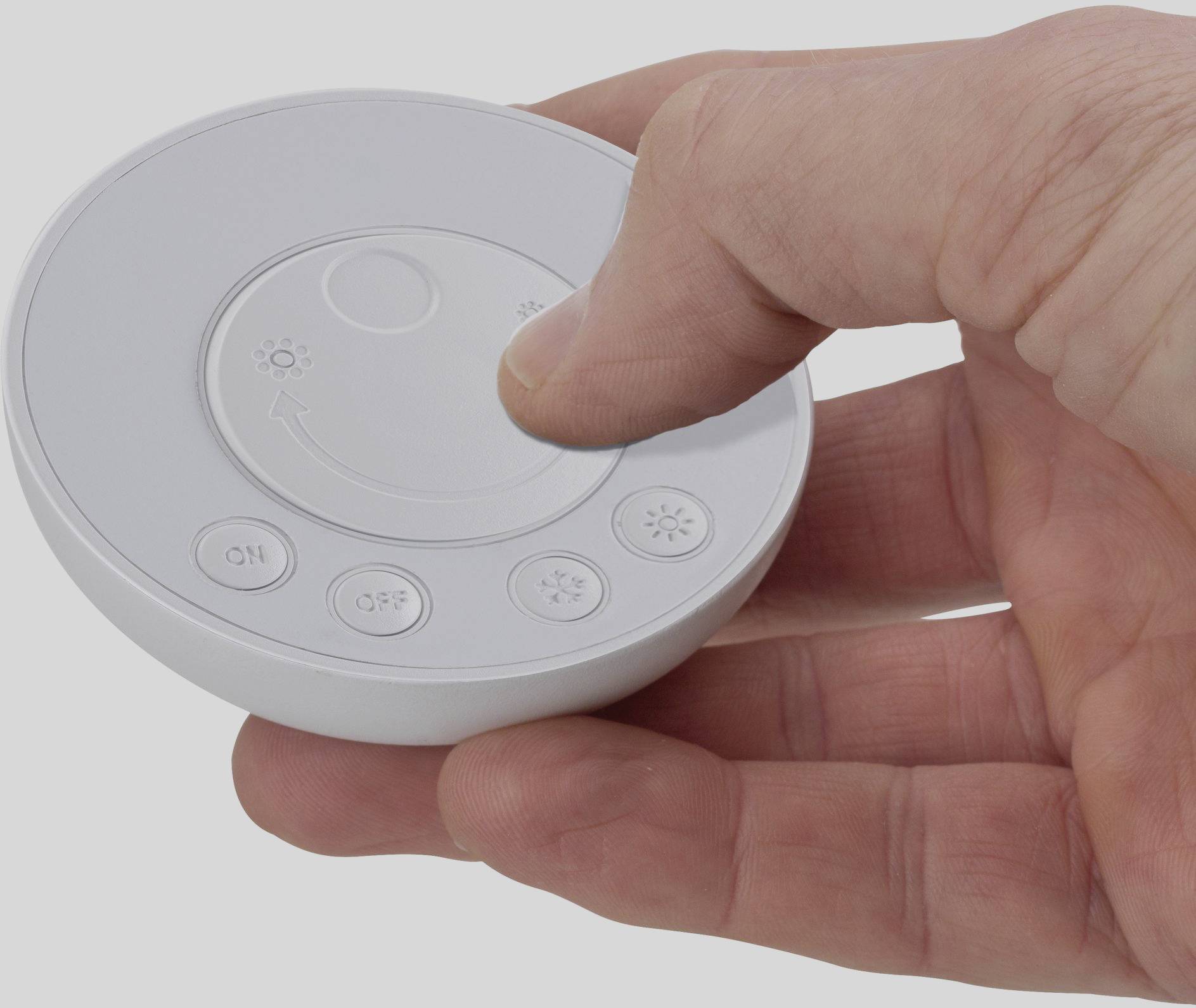 Une main tient une télécommande ronde avec des boutons pour la luminosité et la mise en marche/arrêt. Le pouce appuie sur un bouton.