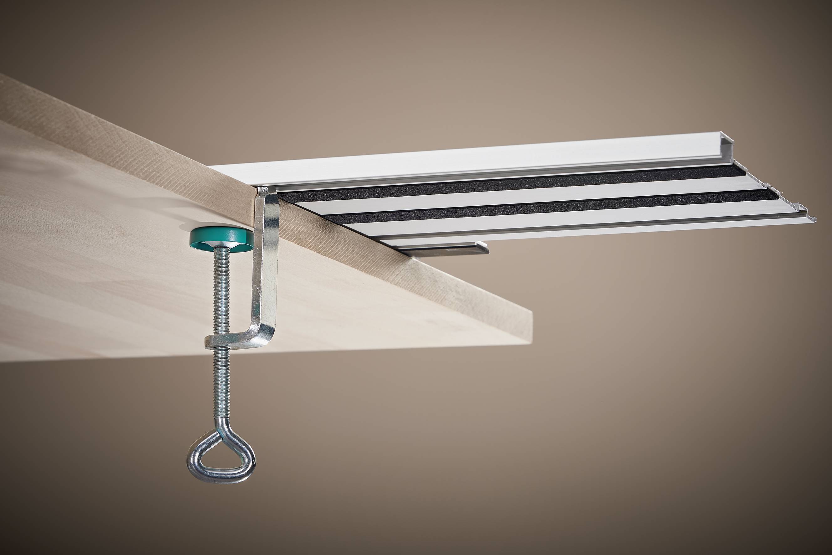 Un serre-joint de bord de table avec une vis verticale et un bouton vert fixe une barre métallique à rayures noires sur le bord d'une table.