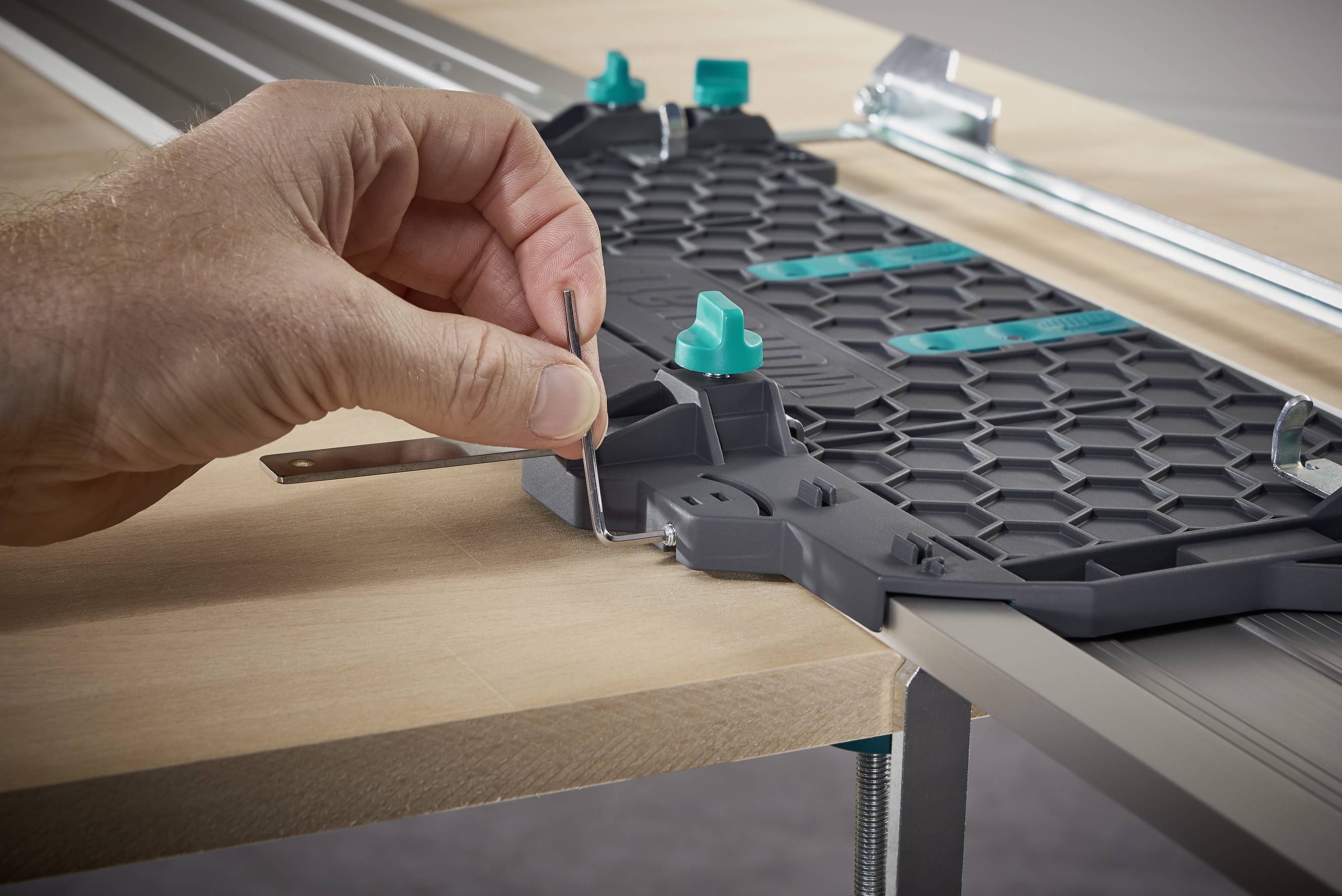 Une main positionne un serre-joint métallique sur une table, utilisé comme partie d'un système d'outillage pour le guidage des fibres de bois.