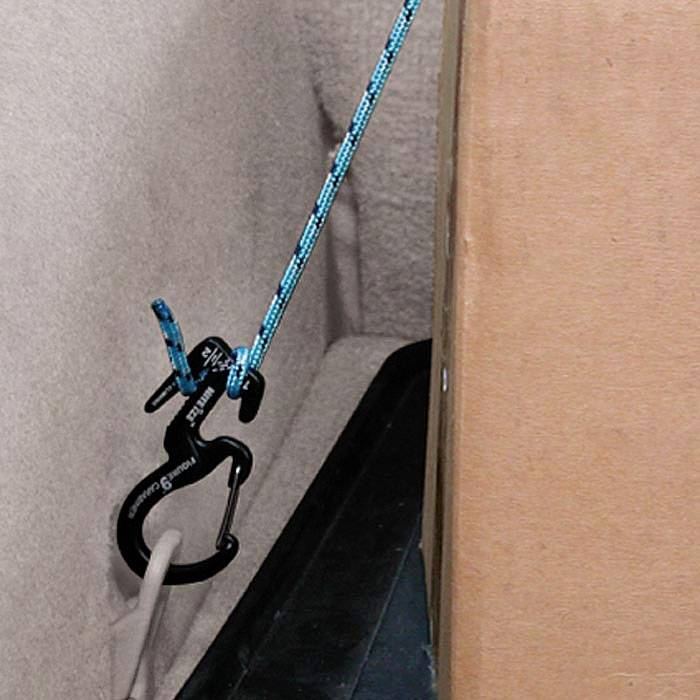 Cordon bleu passé à travers un clip de plastique noir, fixé à un carton ; utilisé pour sécuriser ou attacher.
