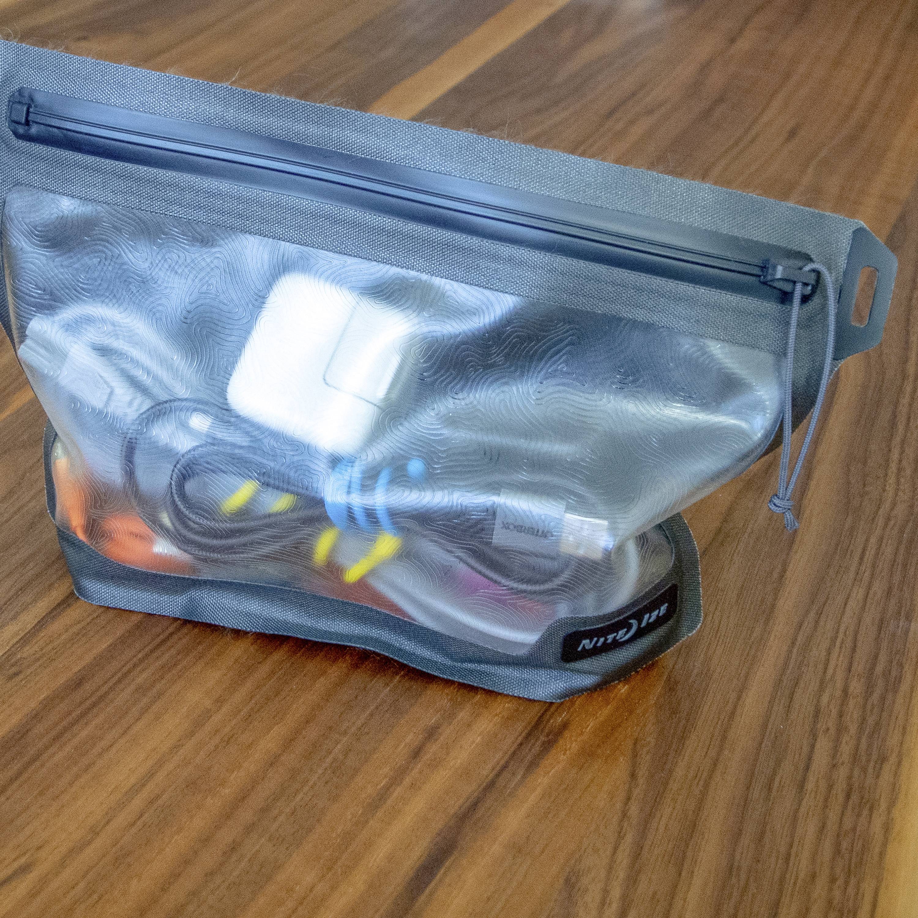 Sac transparent posé sur une table en bois, rempli d'accessoires électroniques tels que des câbles de charge et des adaptateurs.