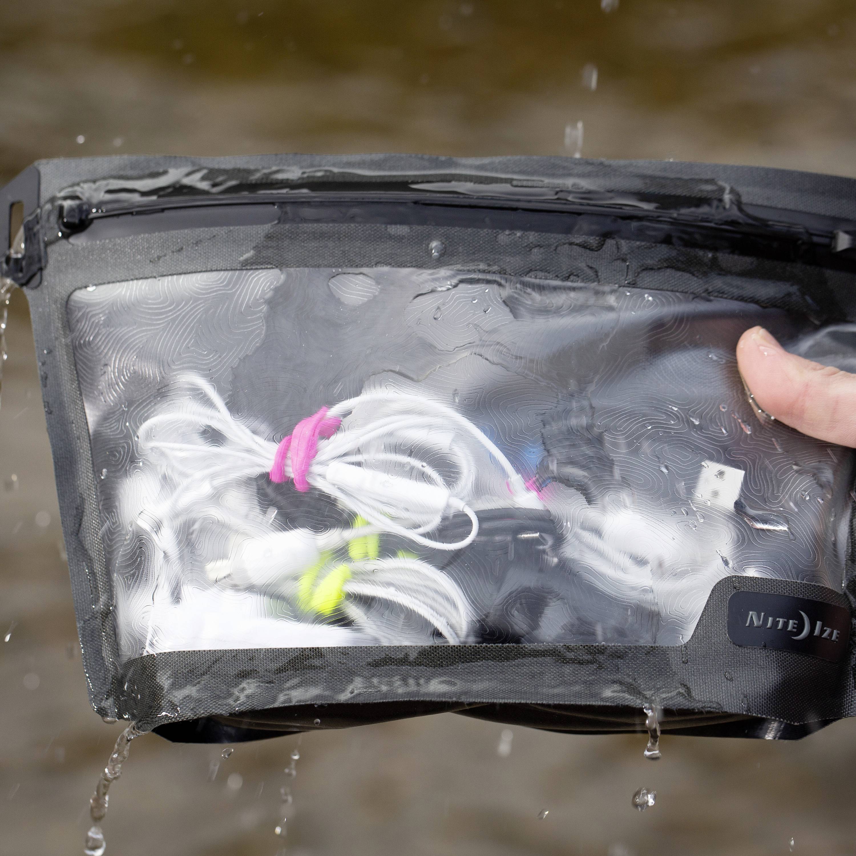Une main tient un sachet transparent et imperméable contenant des écouteurs et un câble à proximité d'un plan d'eau.