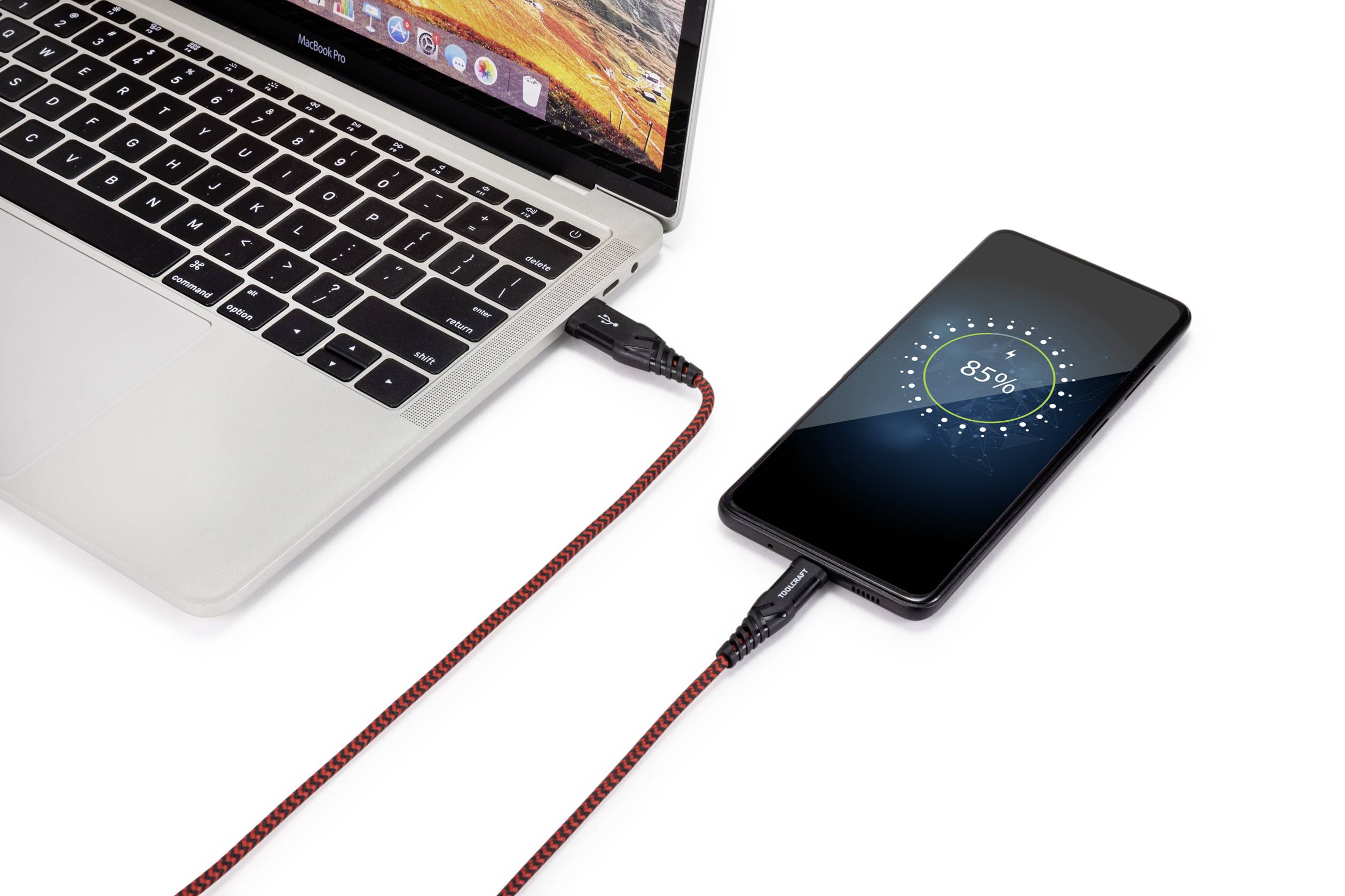 Un smartphone est connecté à un ordinateur portable via un câble rouge et affiche un état de charge de 85 %.