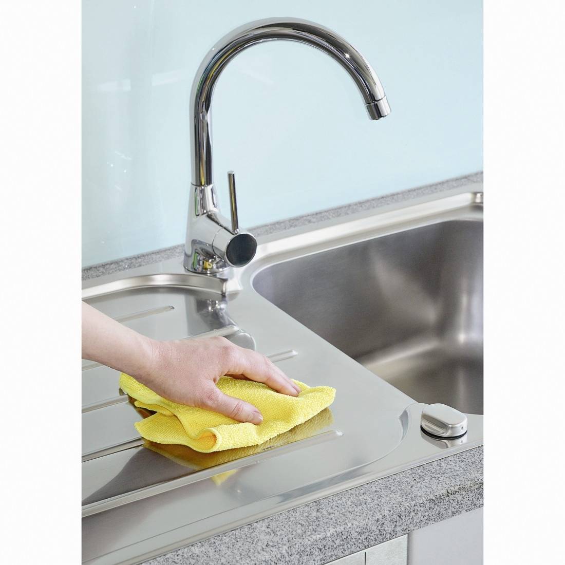 Une main essuie un évier avec un chiffon jaune. Le robinet est en acier inoxydable, et l'environnement semble propre et bien entretenu.
