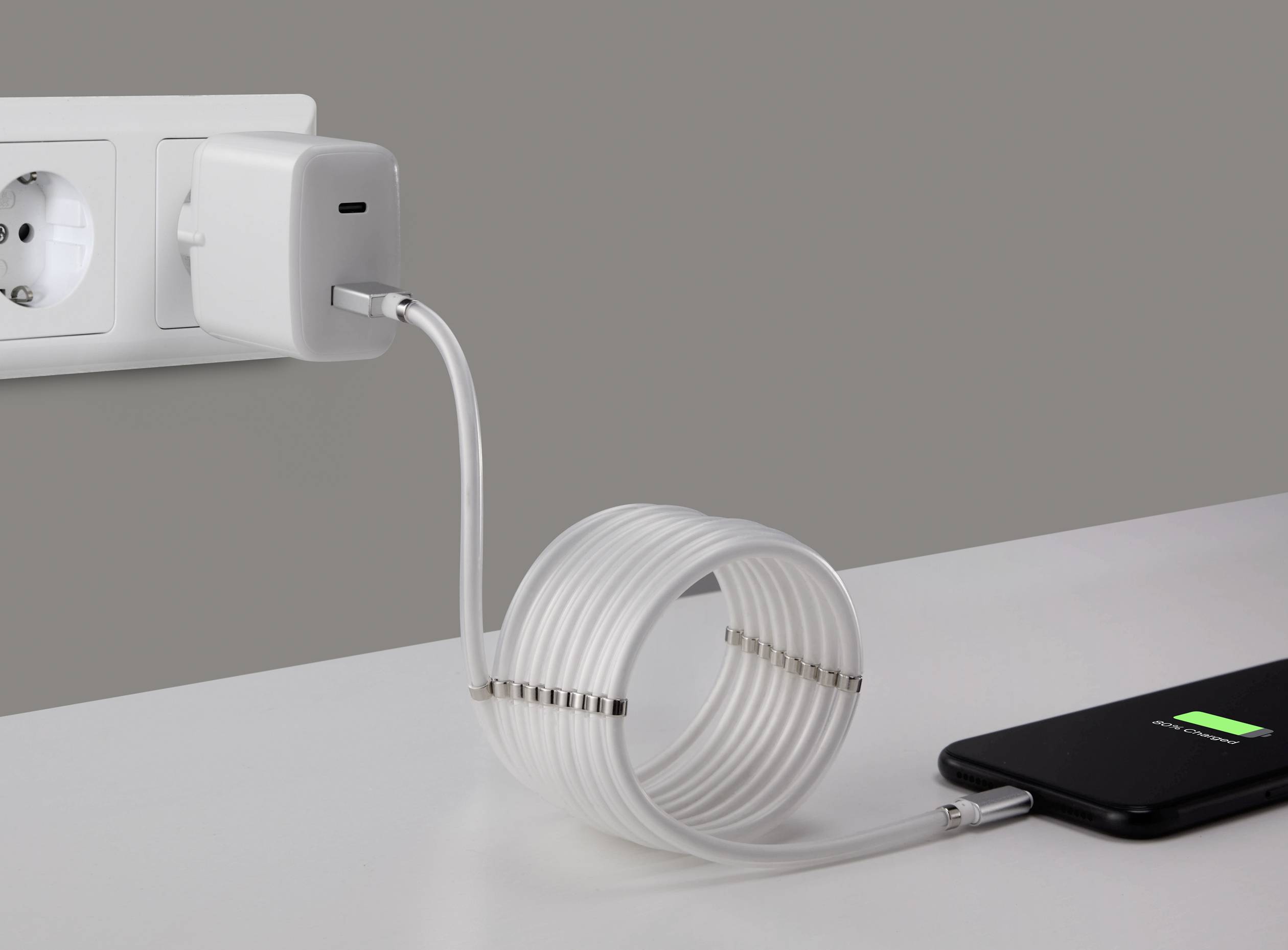 Un smartphone est chargé à l'aide d'un long câble spiralé branché à une prise murale.
