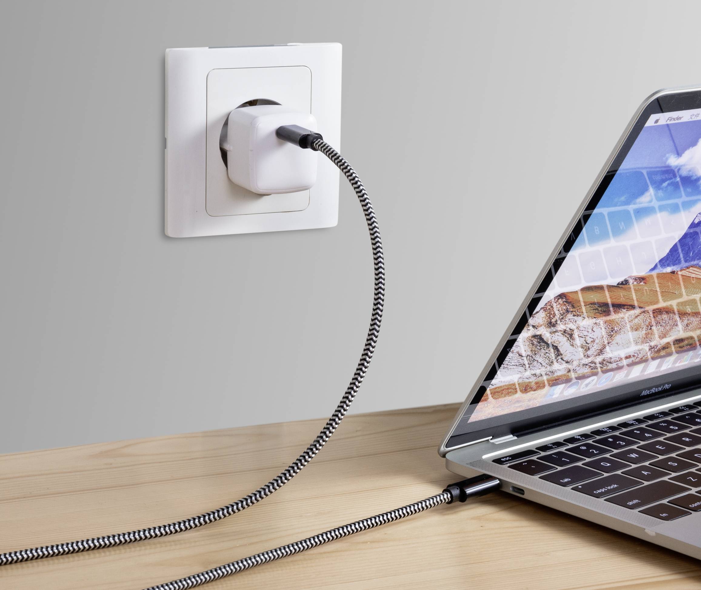 Un ordinateur portable est branché à une prise électrique à l'aide d'un câble d'alimentation. Le câble présente un motif tressé.