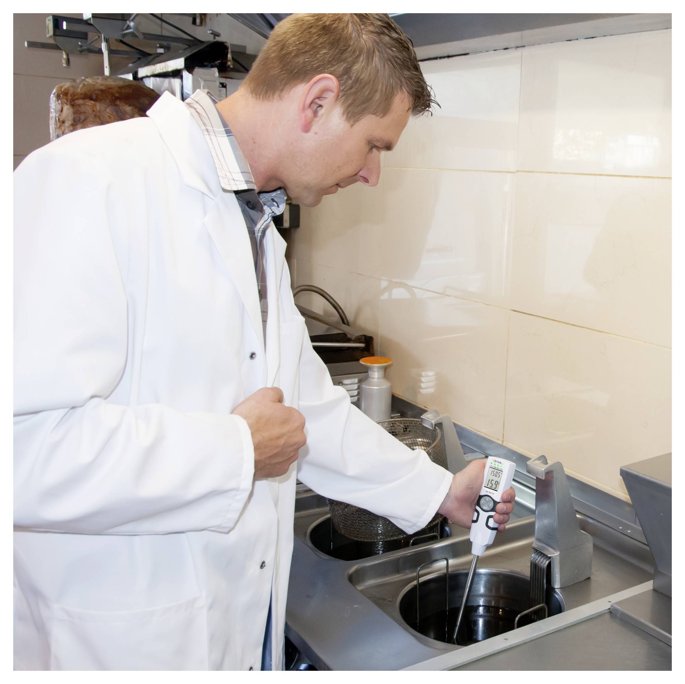 Un homme en blouse de laboratoire blanche utilise un thermomètre portable pour mesurer un liquide dans une casserole de cuisine sur une cuisinière.