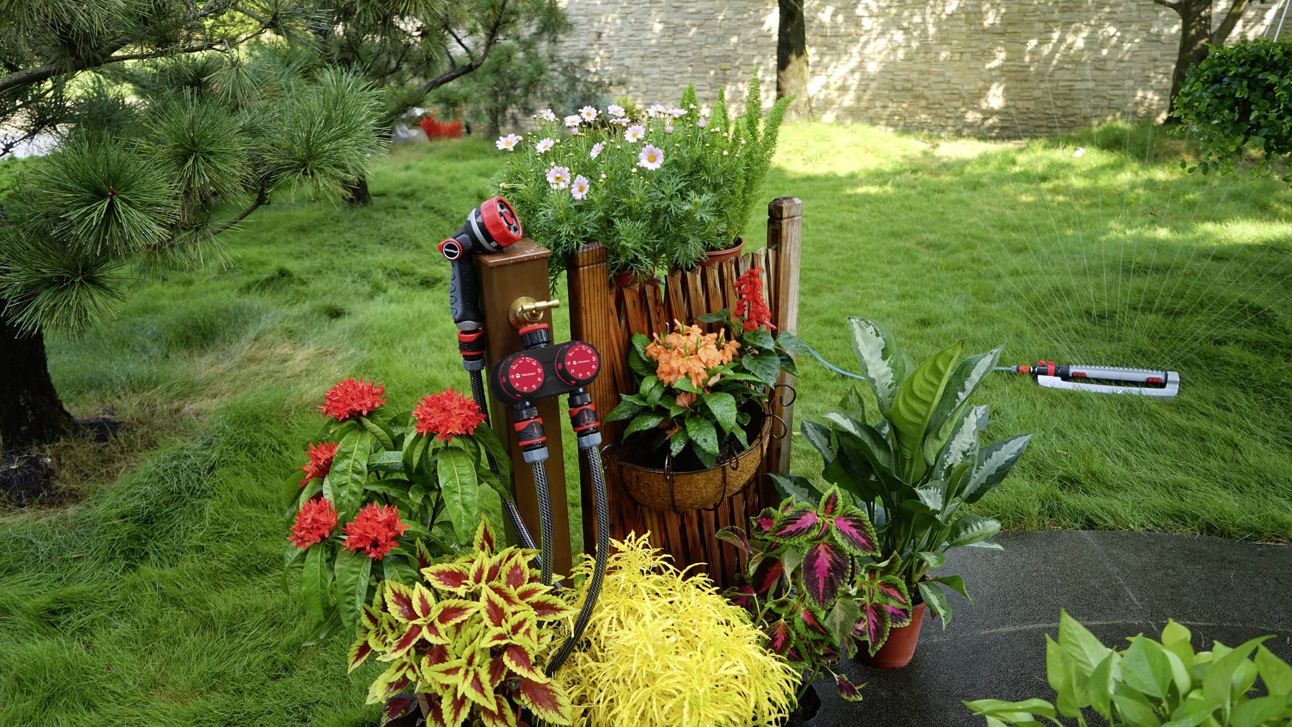 Jardin avec différentes fleurs et plantes colorées, décoré avec un tonneau en bois et des outils de jardinage. Arrière-plan composé de pelouse et d'arbres.