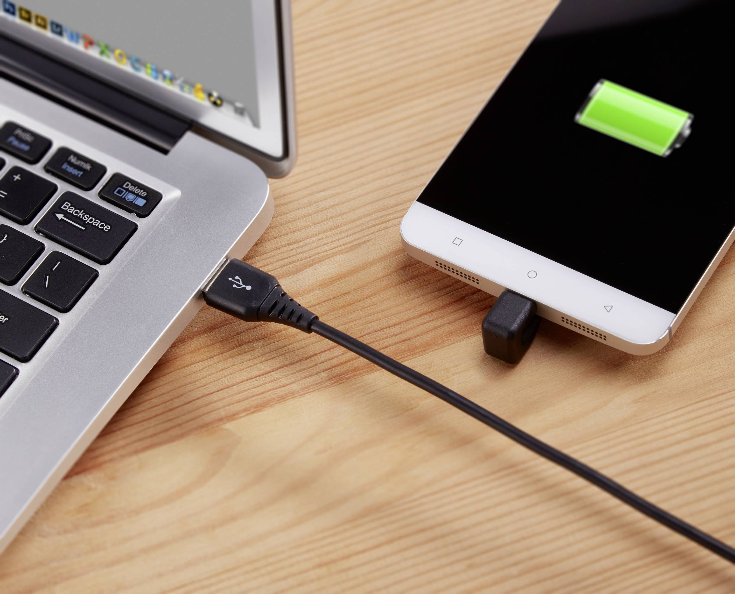 Un smartphone est connecté à un ordinateur portable via un câble USB et en cours de chargement. L'écran du smartphone affiche un symbole de charge vert.