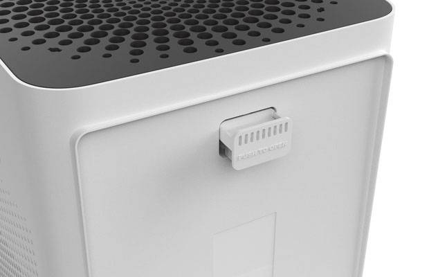 Un purificateur d'air de forme rectangulaire avec un couvercle supérieur noir perforé. Un indicateur de contrôle est situé sur le côté.