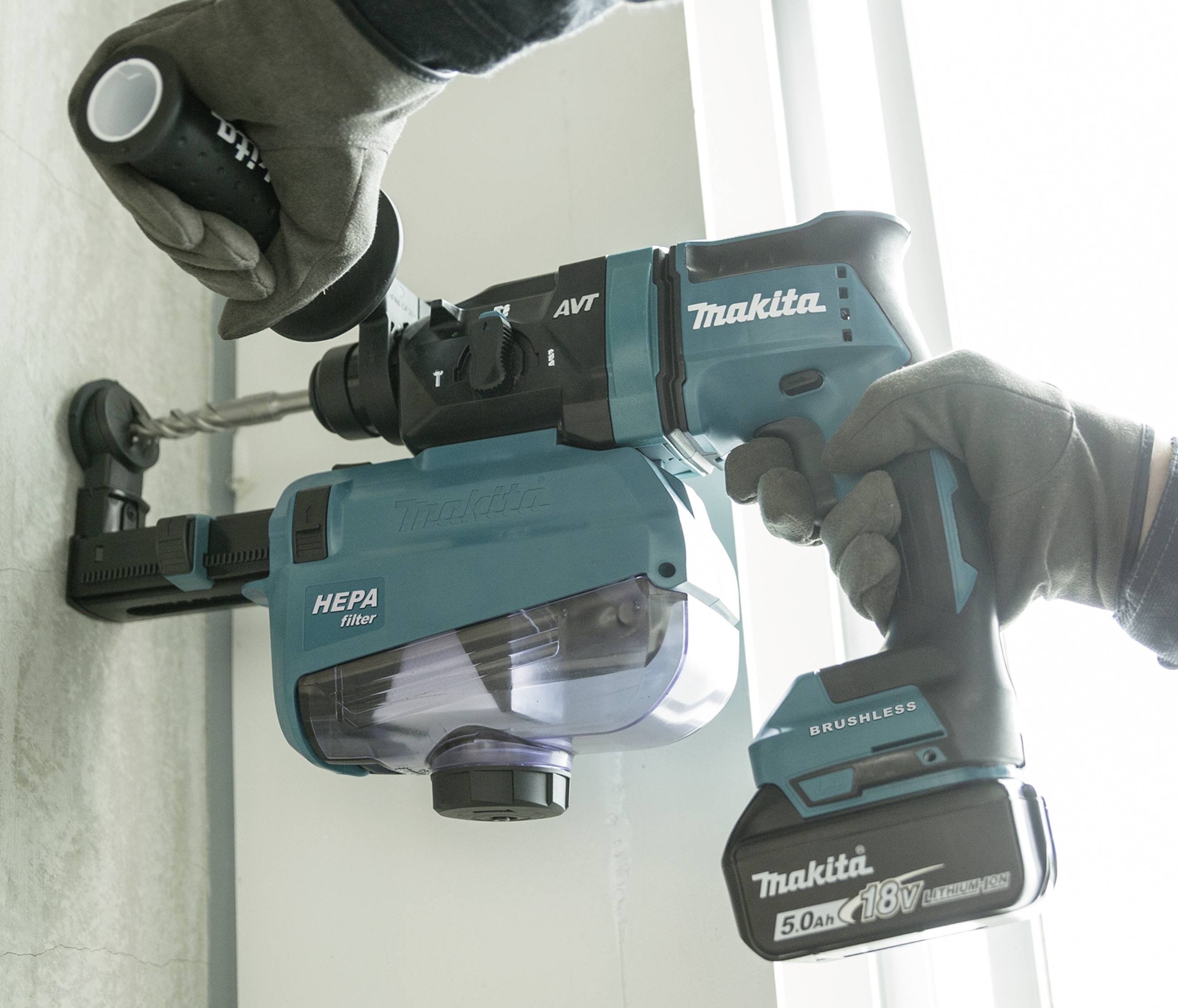 Une personne fore un mur à l'aide d'un marteau perforateur sans fil Makita. La poussière est captée par un filtre HEPA intégré.