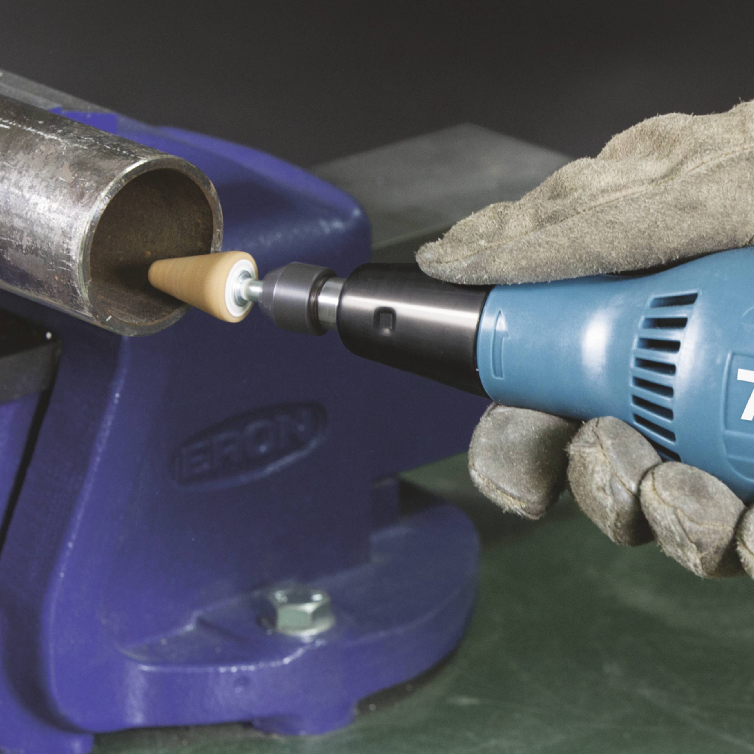 Une personne portant des gants de travail utilise une polisseuse électrique pour polir une pièce métallique.