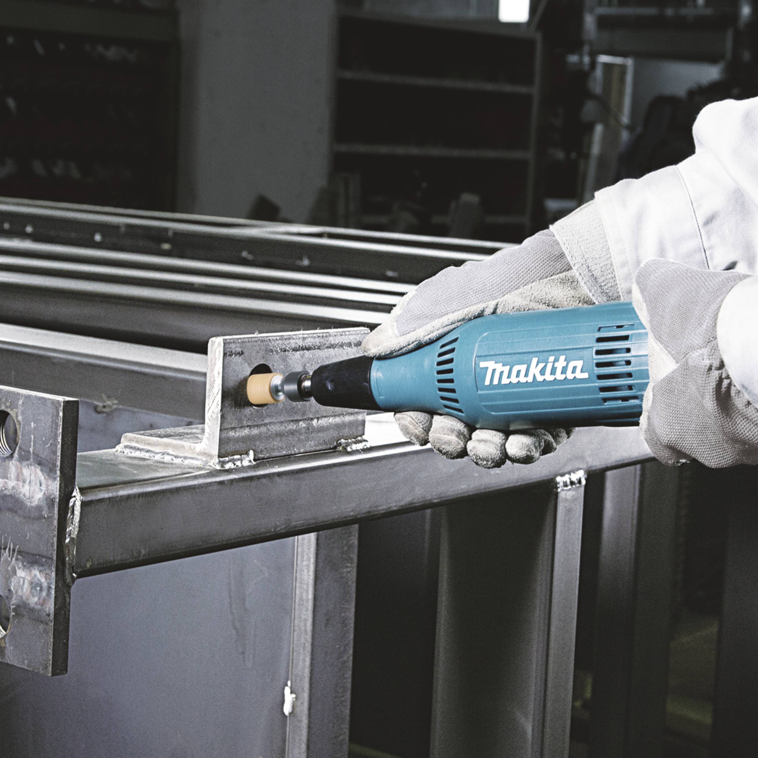 Une personne utilise un outil bleu clair de Makita pour poncer les bords métalliques d'un châssis en acier.