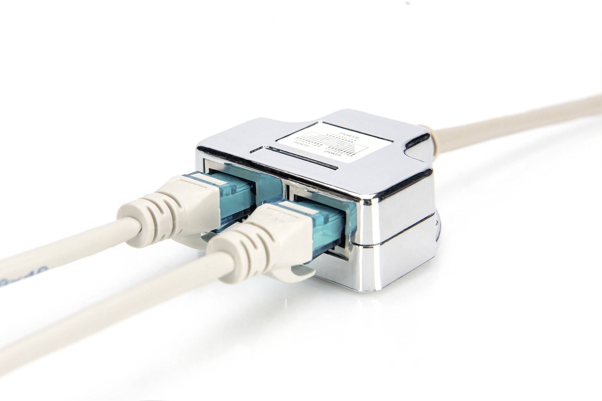 Deux câbles Ethernet beiges sont branchés dans un répartiteur réseau argenté, posé sur une surface blanche.