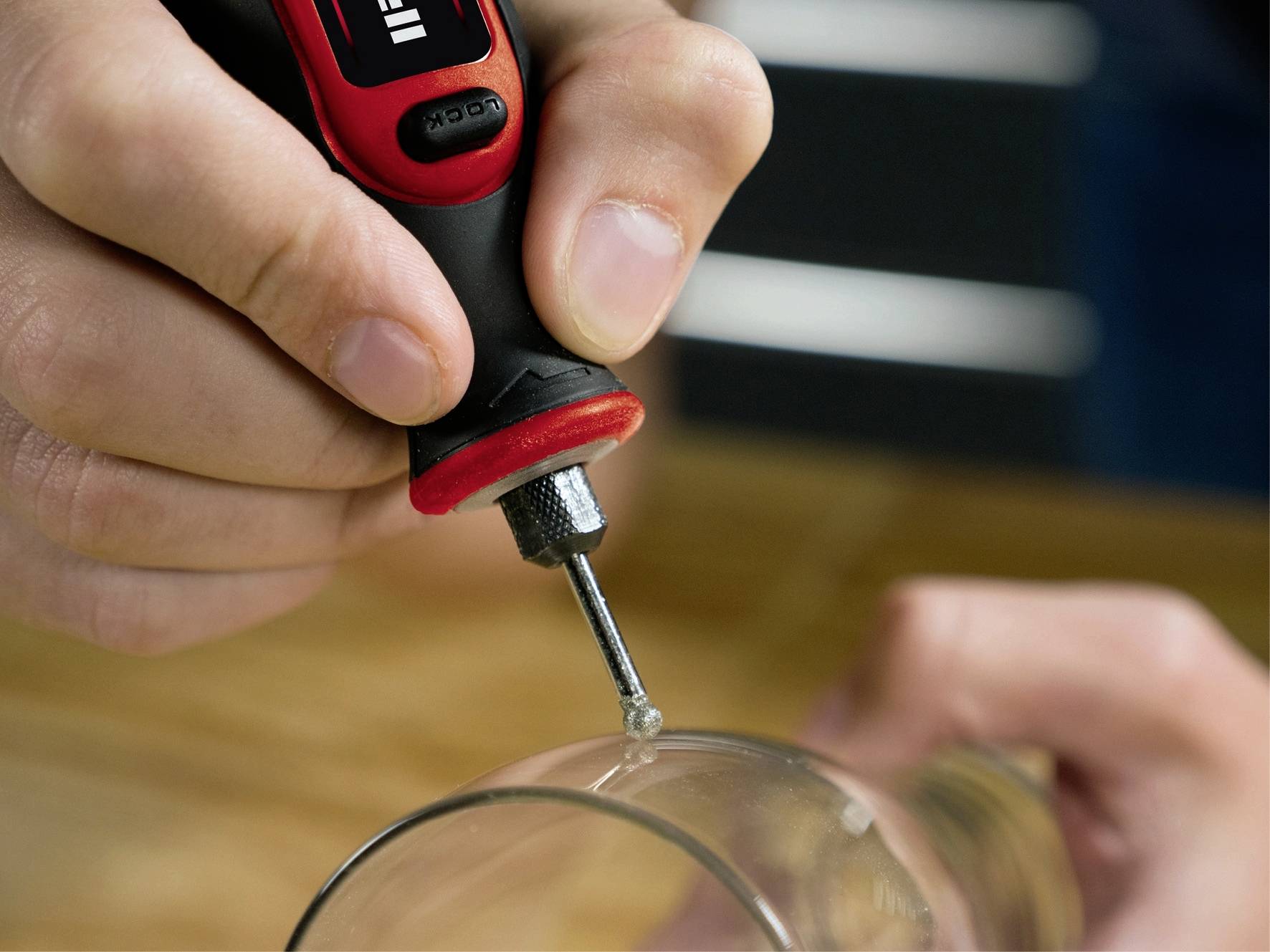 Une personne utilise un fer à souder rouge et noir pour effectuer une petite réparation sur un objet en verre.