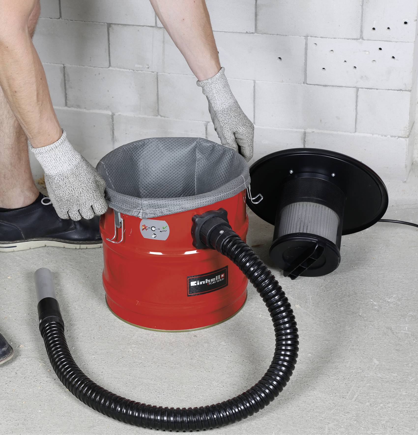 Une personne est en train de monter un aspirateur à cendres. Le récipient rouge est ouvert à côté d'un tuyau noir et d'un couvercle de filtre.