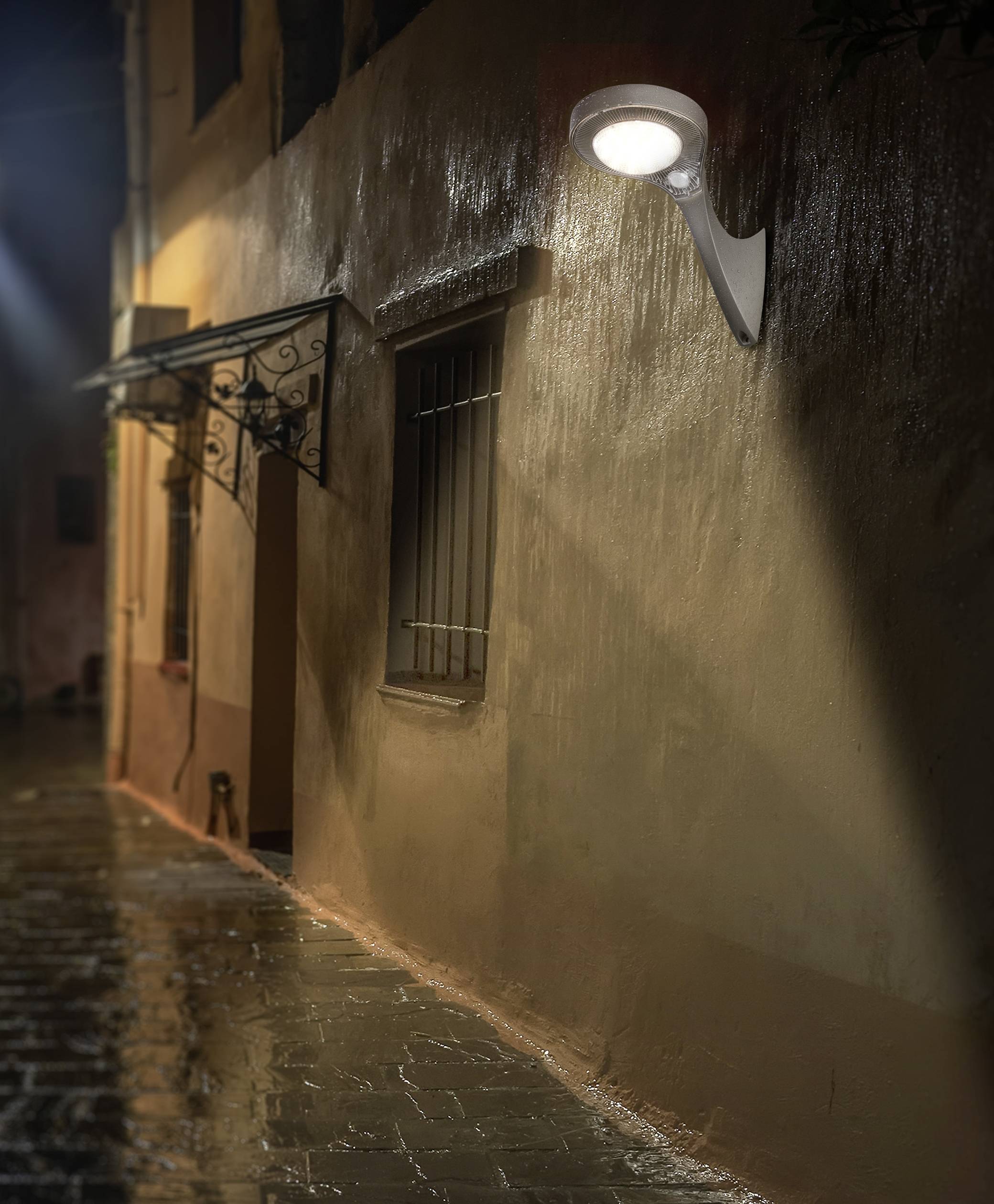 Une ruelle éclairée la nuit. Un réverbère projette une lumière chaleureuse sur une rue humide et déserte, longeant un bâtiment.