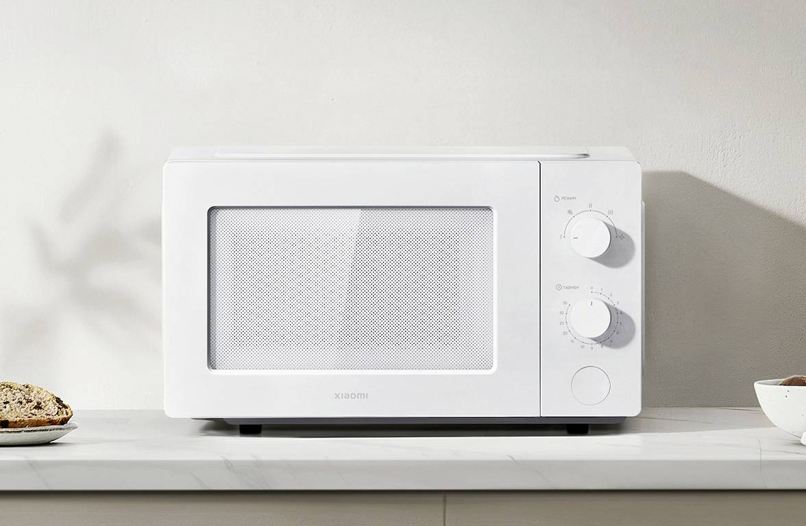 Four à micro-ondes blanc sur un plan de travail de cuisine, avec deux boutons rotatifs sur le côté droit, dans un environnement de design intérieur minimaliste.