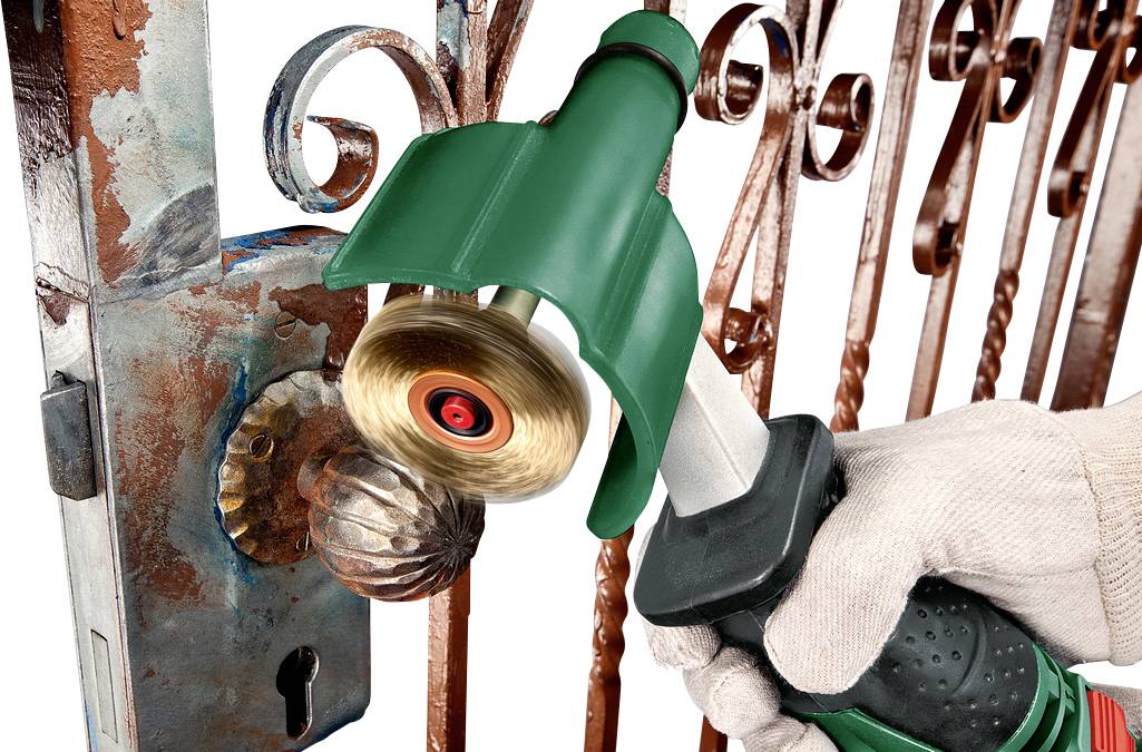 Une personne polit un portail métallique rouillé à l'aide d'une brosse métallique électrique. L'accent est mis sur le nettoyage de la poignée de la porte.