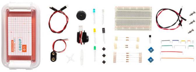 Kit électronique avec plaque d'expérimentation, câbles, interrupteurs et divers composants électroniques sur un fond blanc.