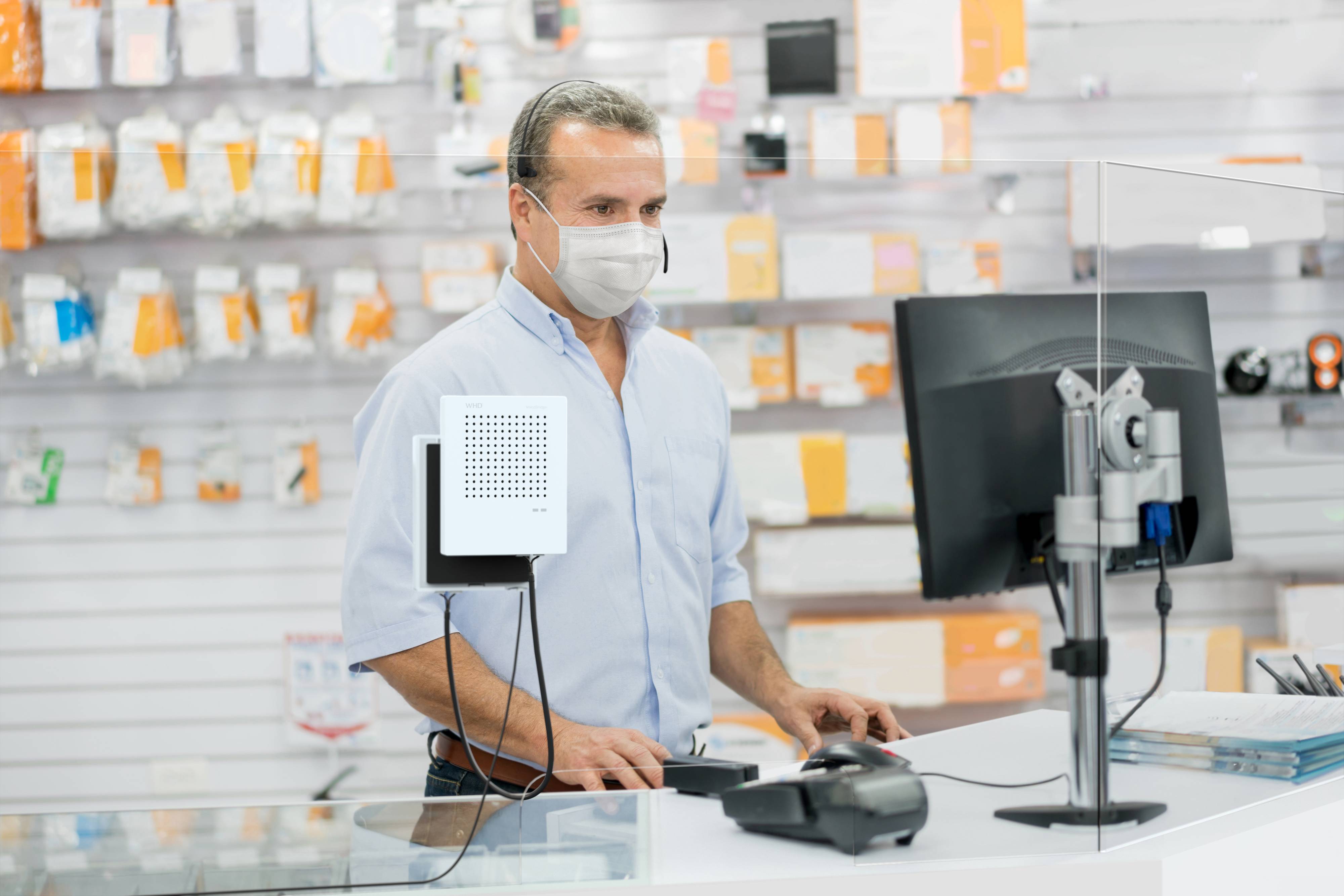 Un homme portant un masque utilise un ordinateur dans un magasin. À l'arrière-plan, divers articles électroniques sont visibles.