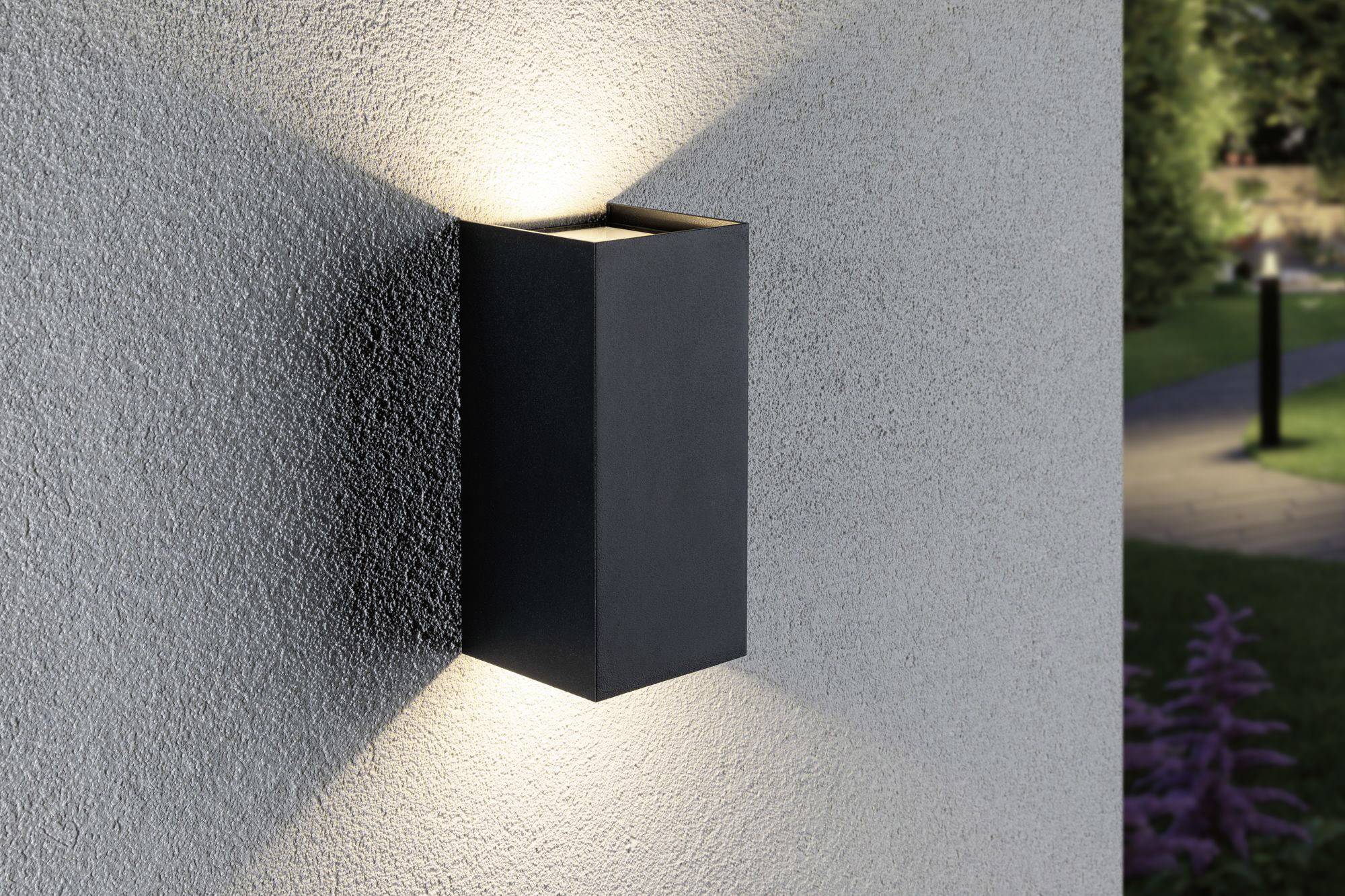 Un luminaire mural moderne au design rectangulaire diffuse de la lumière vers le haut et vers le bas, installé sur un mur gris.