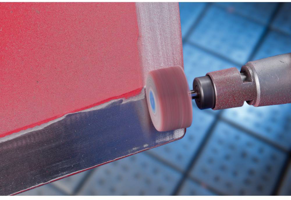 Un outil de meulage rotatif qui lisse le bord d'un matériau rouge. L'arrière-plan présente un motif quadrillé bleu.