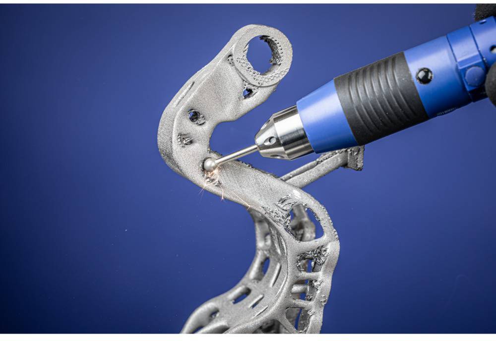 Un objet imprimé en 3D est usiné par un outil à main bleu sur un fond bleu.