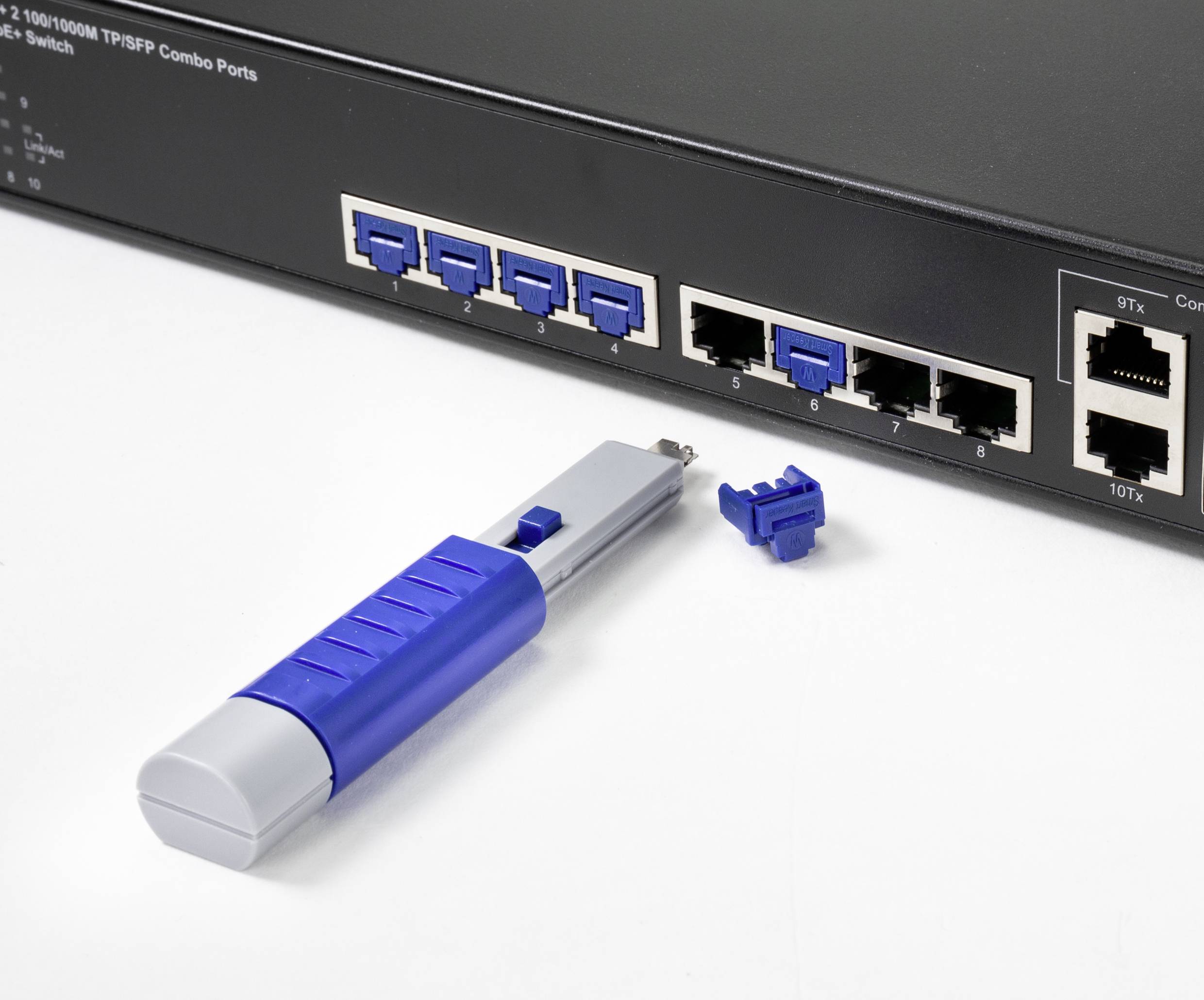 Un commutateur réseau avec des ports bleus, un outil de fibre optique et deux capuchons de connecteur bleus sur un fond blanc.