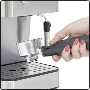 Une main tient un porte-filtre noir qui est inséré dans une machine à espresso argentée. Surface en bois en arrière-plan.
