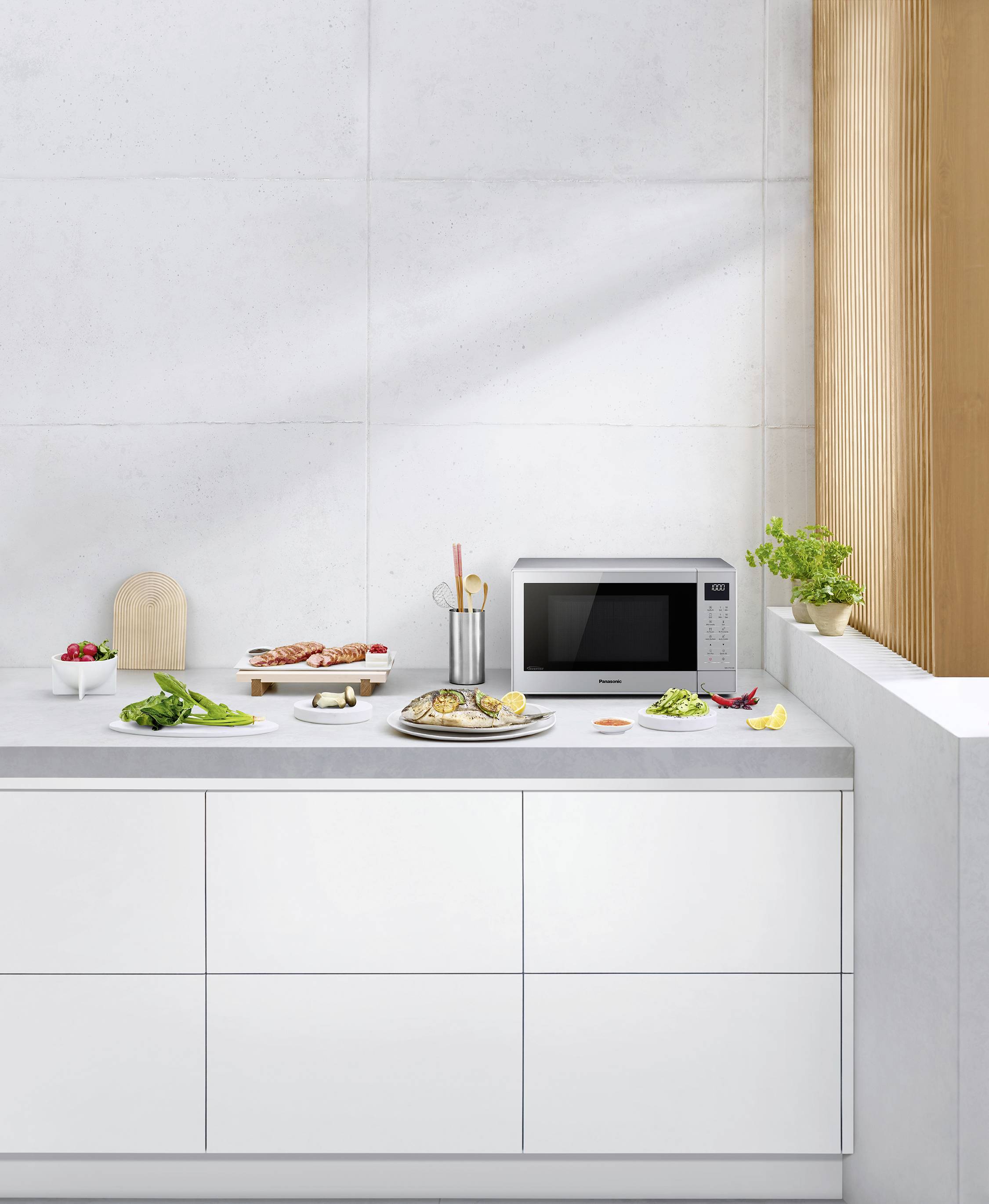 Une cuisine moderne avec des armoires blanches, sur lesquelles sont disposés des légumes, des herbes, un micro-ondes et des ustensiles de cuisine.