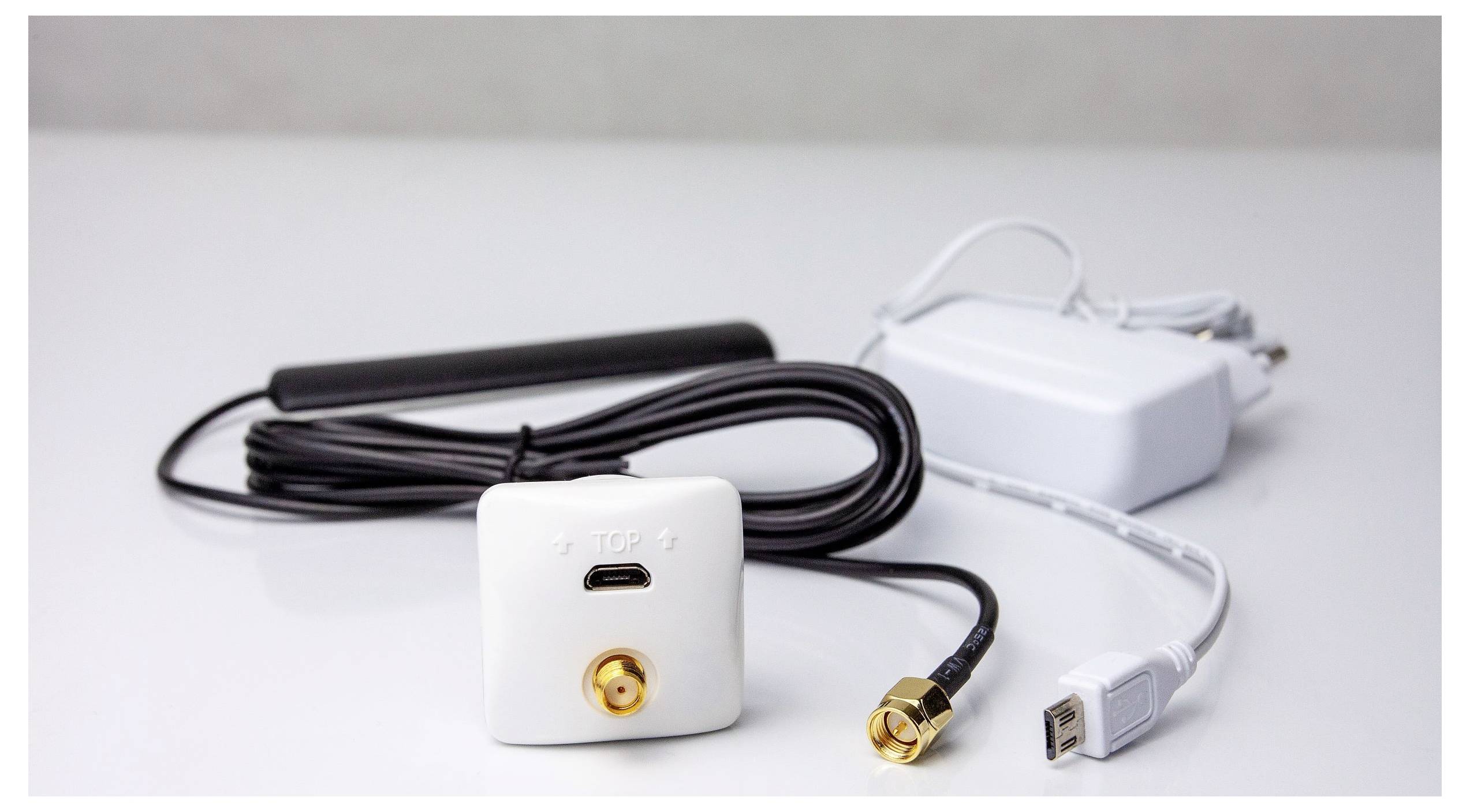 Un appareil réseau blanc avec des câbles et une antenne, présentant un connecteur doré et un port USB, placé sur une surface blanche.