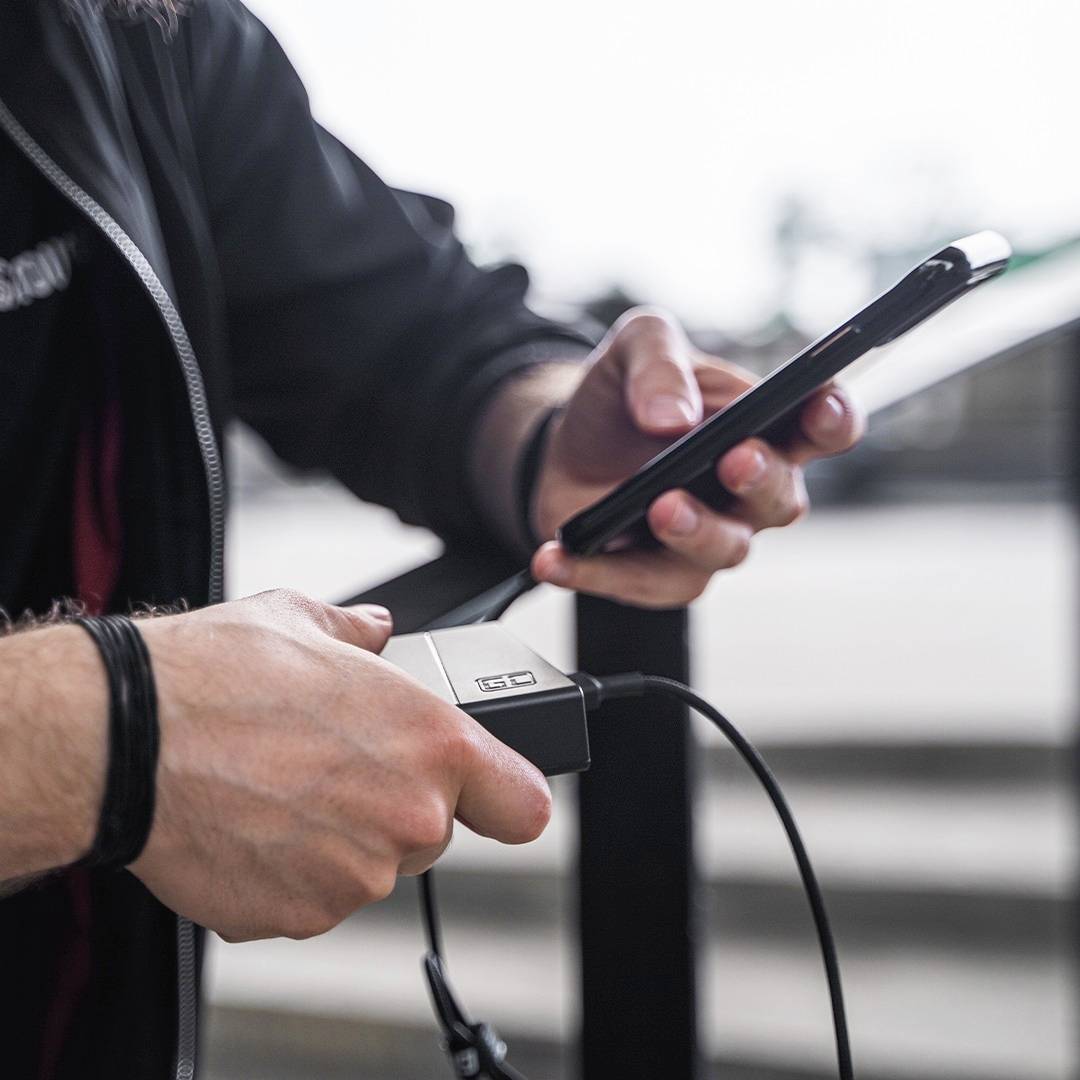 Une personne charge son smartphone avec une batterie externe alors qu'elle se trouve à l'extérieur. Aucun autre détail ou contexte n'est visible.