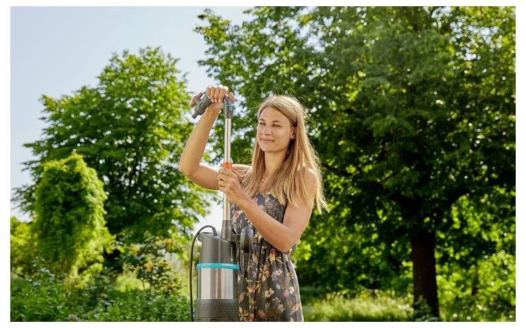 Femme utilisant une pompe à eau manuelle ou un vaporisateur de jardin à l'extérieur dans un jardin verdoyant ensoleillé.