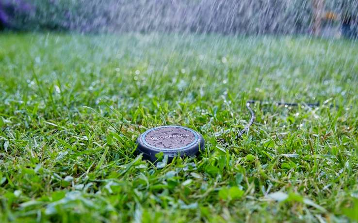 Un arroseur arrose une pelouse verdoyante et luxuriante, avec des gouttelettes d'eau tombant visiblement, créant une scène de jardin fraîche et vivante.