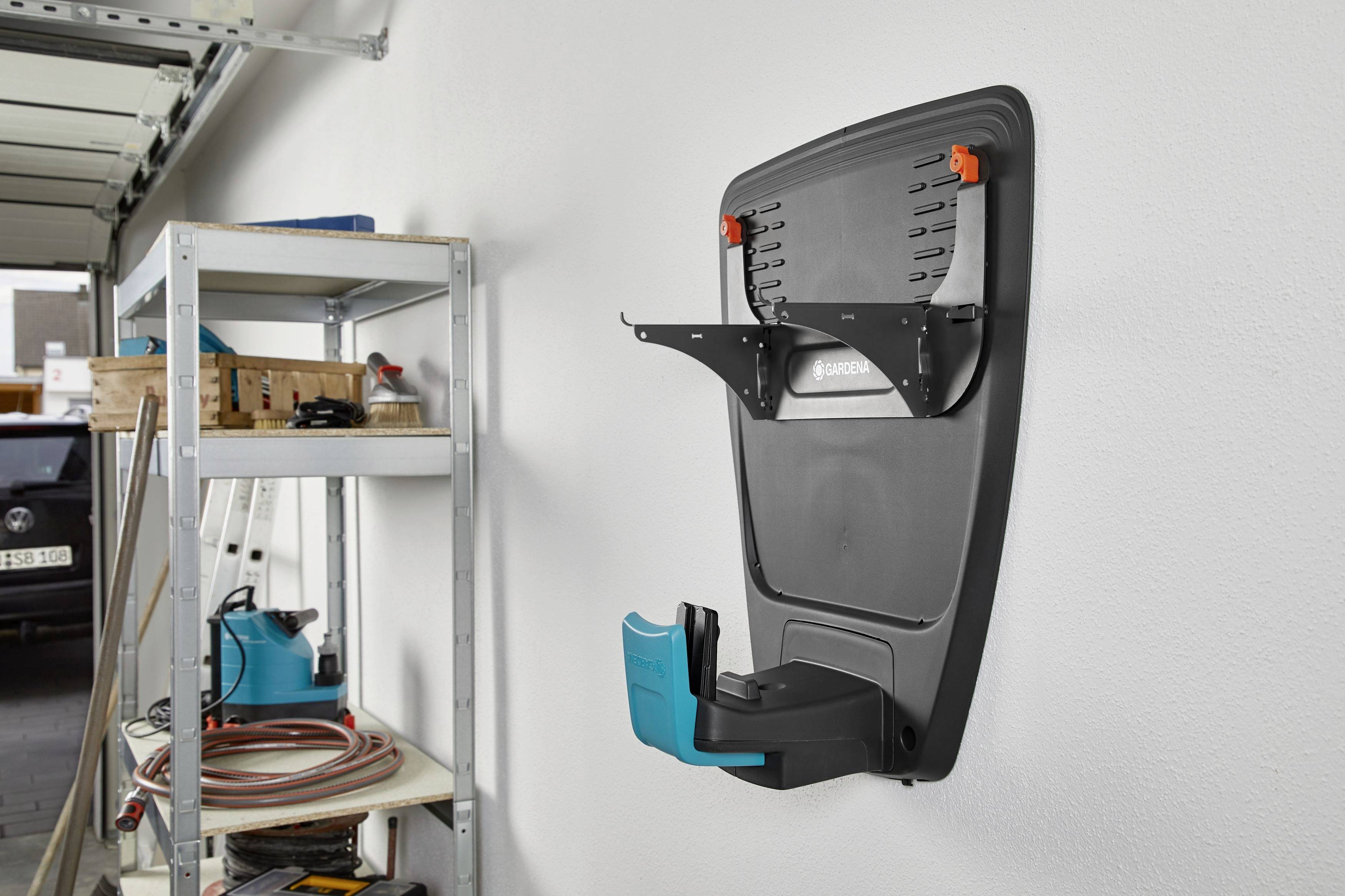 Sur le mur d'un garage, on peut voir un chargeur installé avec un support de câble. À gauche se trouve une étagère avec des outils et des rouleaux de câbles.
