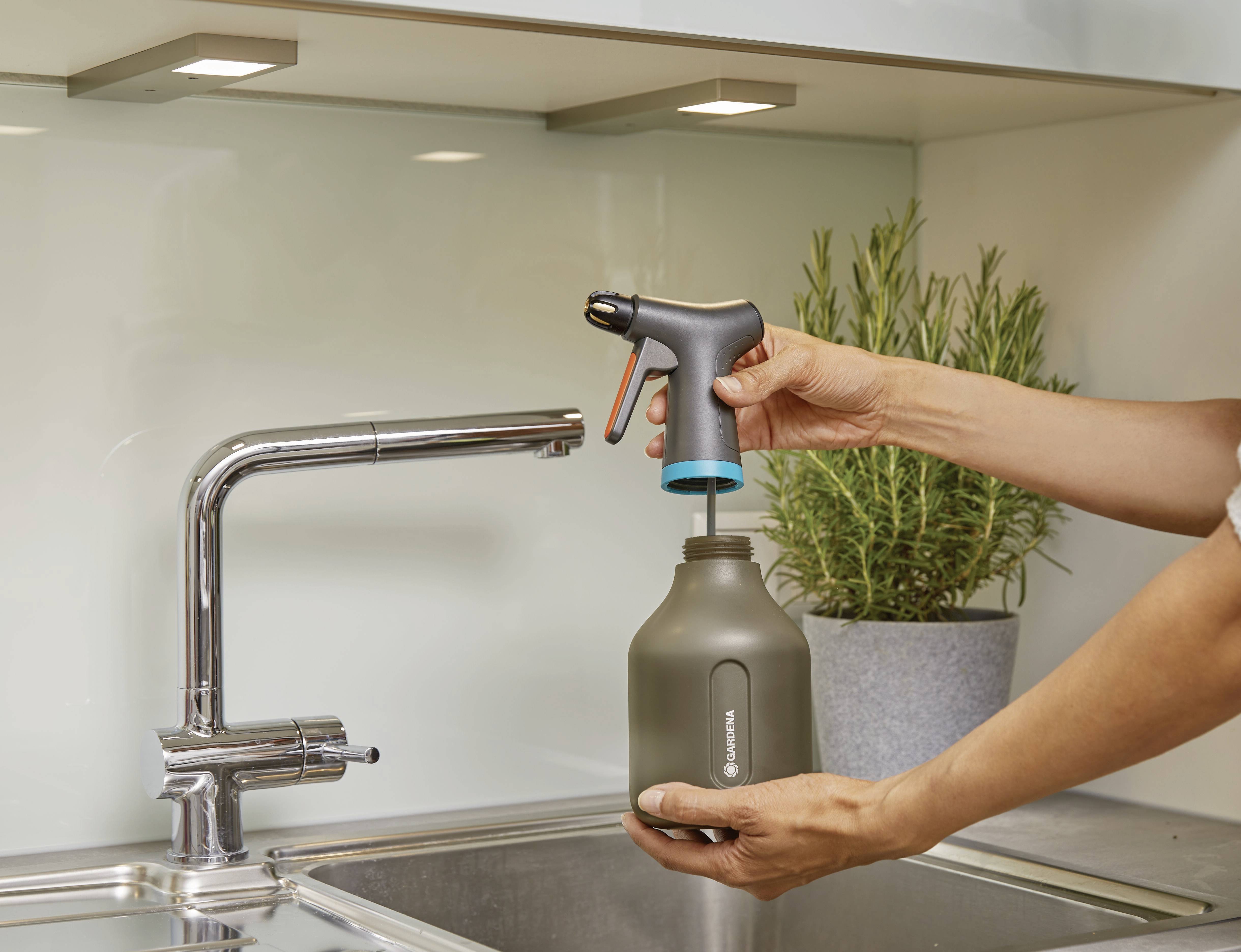 Une personne installe une machine à gazéifier l'eau sur une bouteille d'eau dans un environnement de cuisine. Une plante est visible en arrière-plan.