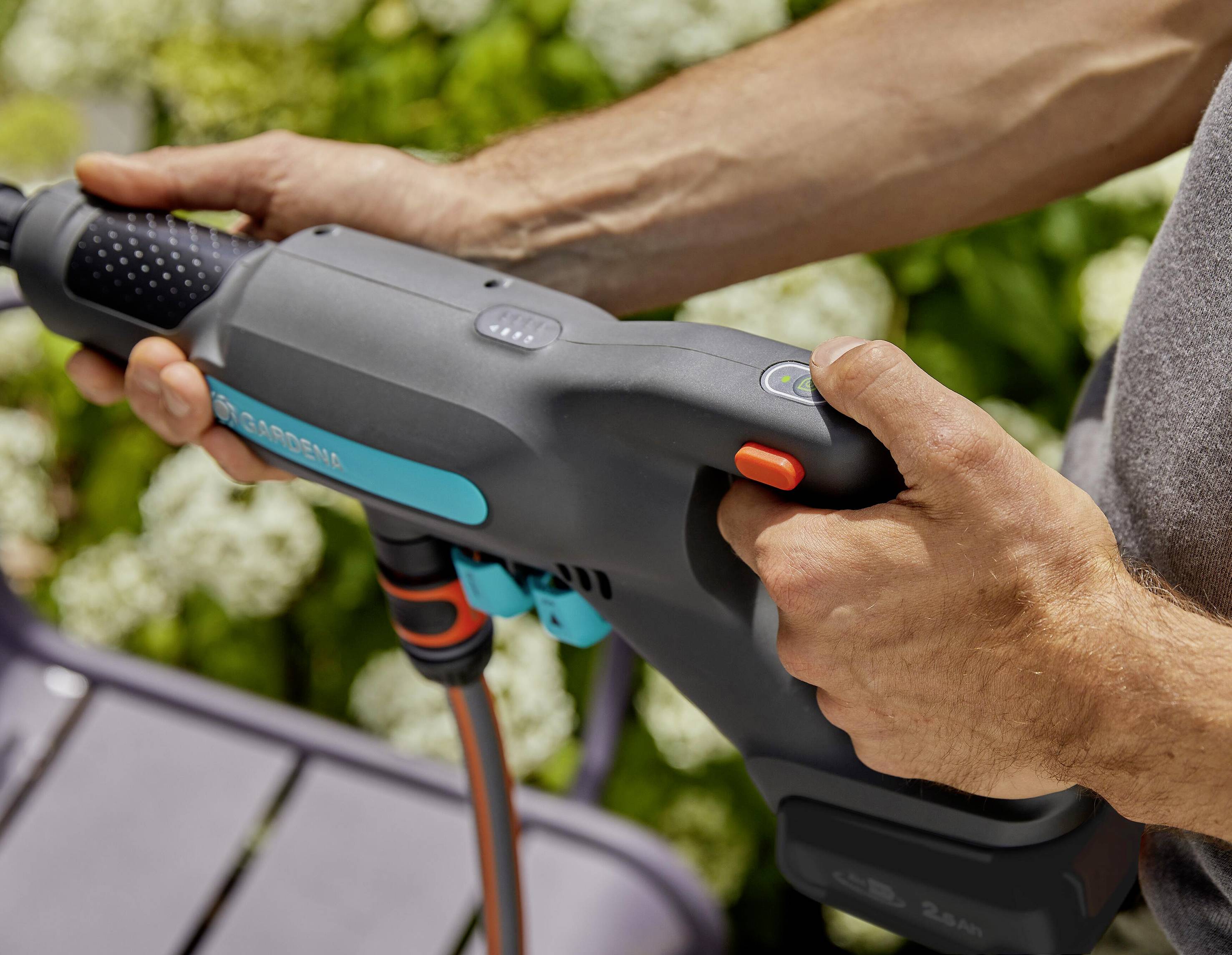 Une personne tient un nettoyeur haute pression dans ses mains, prête à l'utiliser dans le jardin. Des plantes vertes sont visibles en arrière-plan.